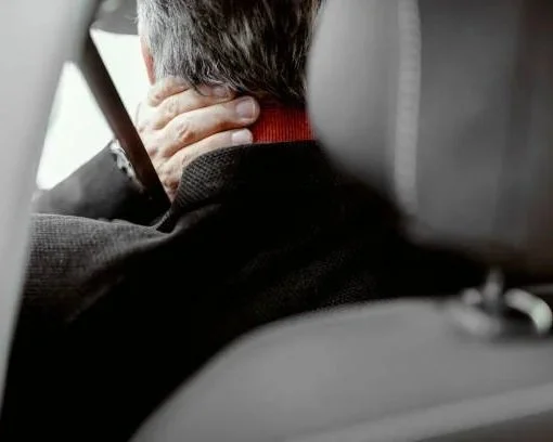 Person sitting in a car, holding their neck in discomfort or pain wanting medico-legal service such as soft tissue whip lash injury via MedCo