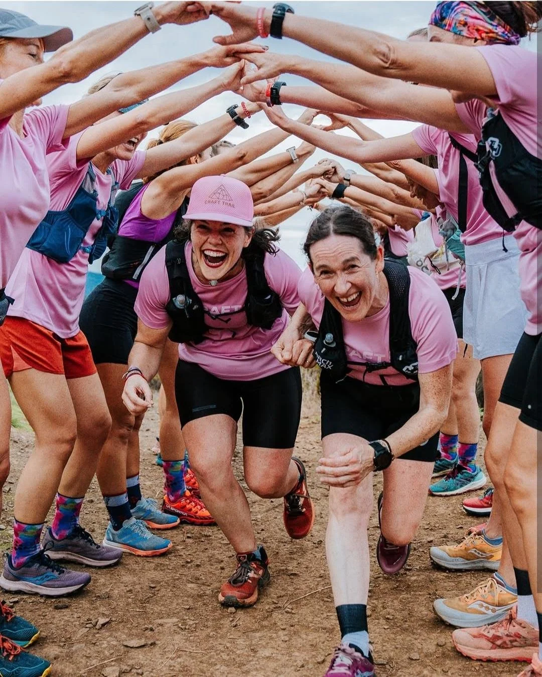 Group of women participating in a team outdoor run, forming a tunnel with their arms, smiling and cheering at the camera.