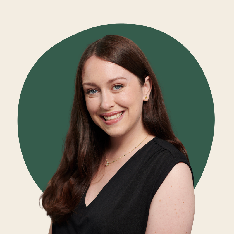 Jesika Arseneau | A woman with long brown hair wearing a black sleeveless top and gold jewelry, smiling in front of a circular green background.