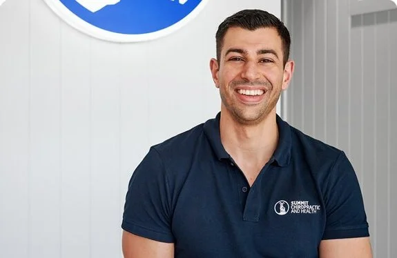 A man wearing a navy blue polo shirt with a logo, smiling in an indoor setting.