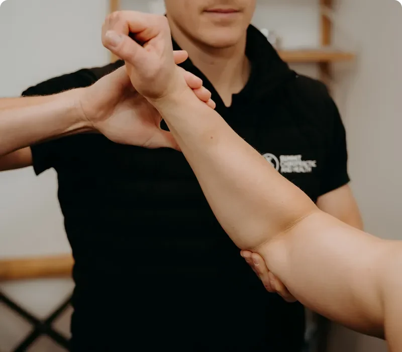 Person receiving physical therapy on their elbow from a therapist in a clinic setting.