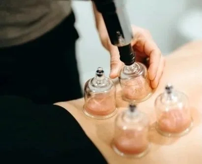 A person holding a tool over small glass bowls on a table, possibly for a skincare or cosmetic treatment.