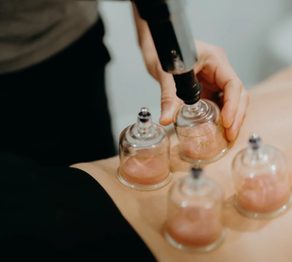 Person holding a small glass bottle and using a dropper to transfer liquid into it, with other similar bottles on the table.