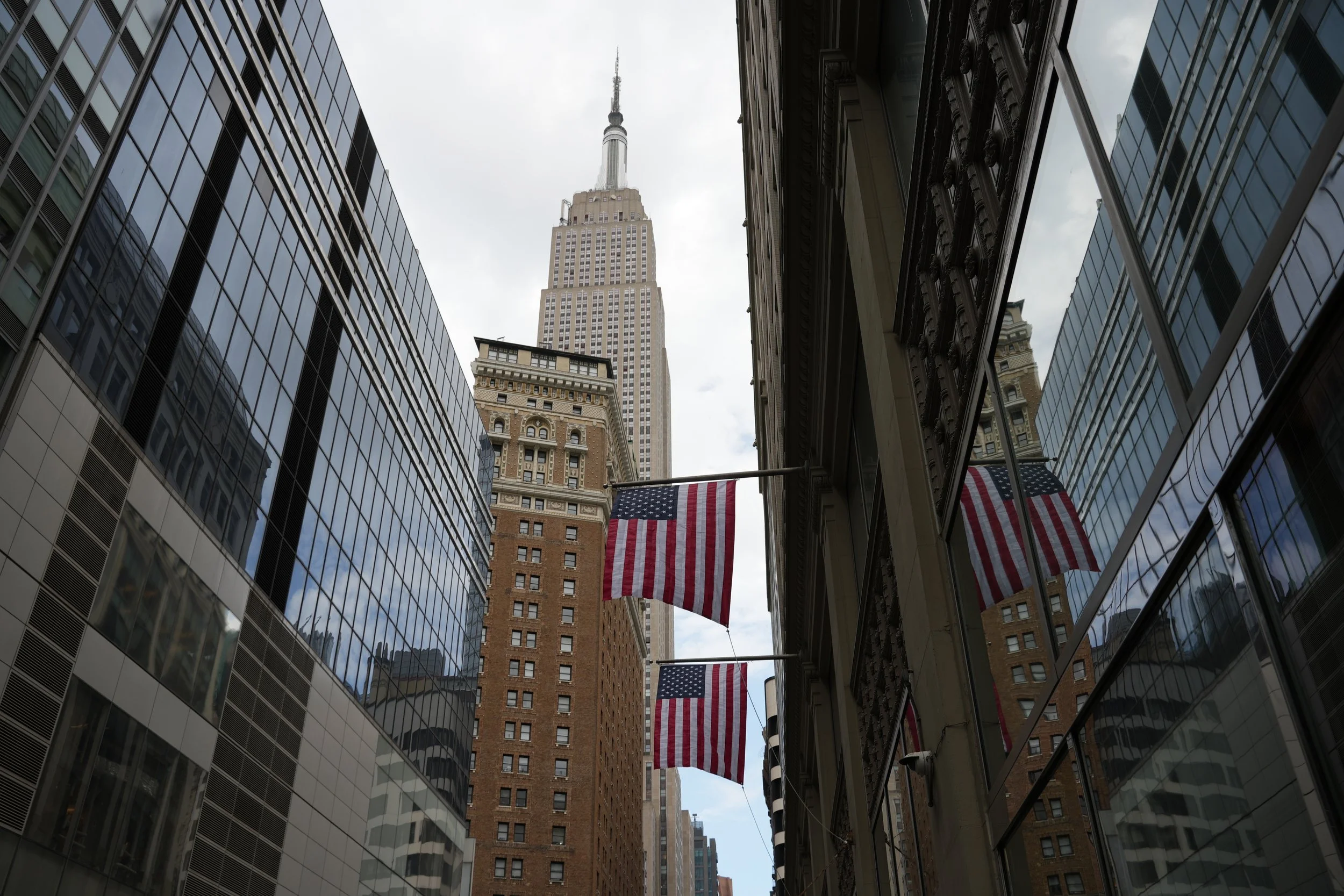 American flags hanging between modern glass buildings with the Empire State Building in the background.