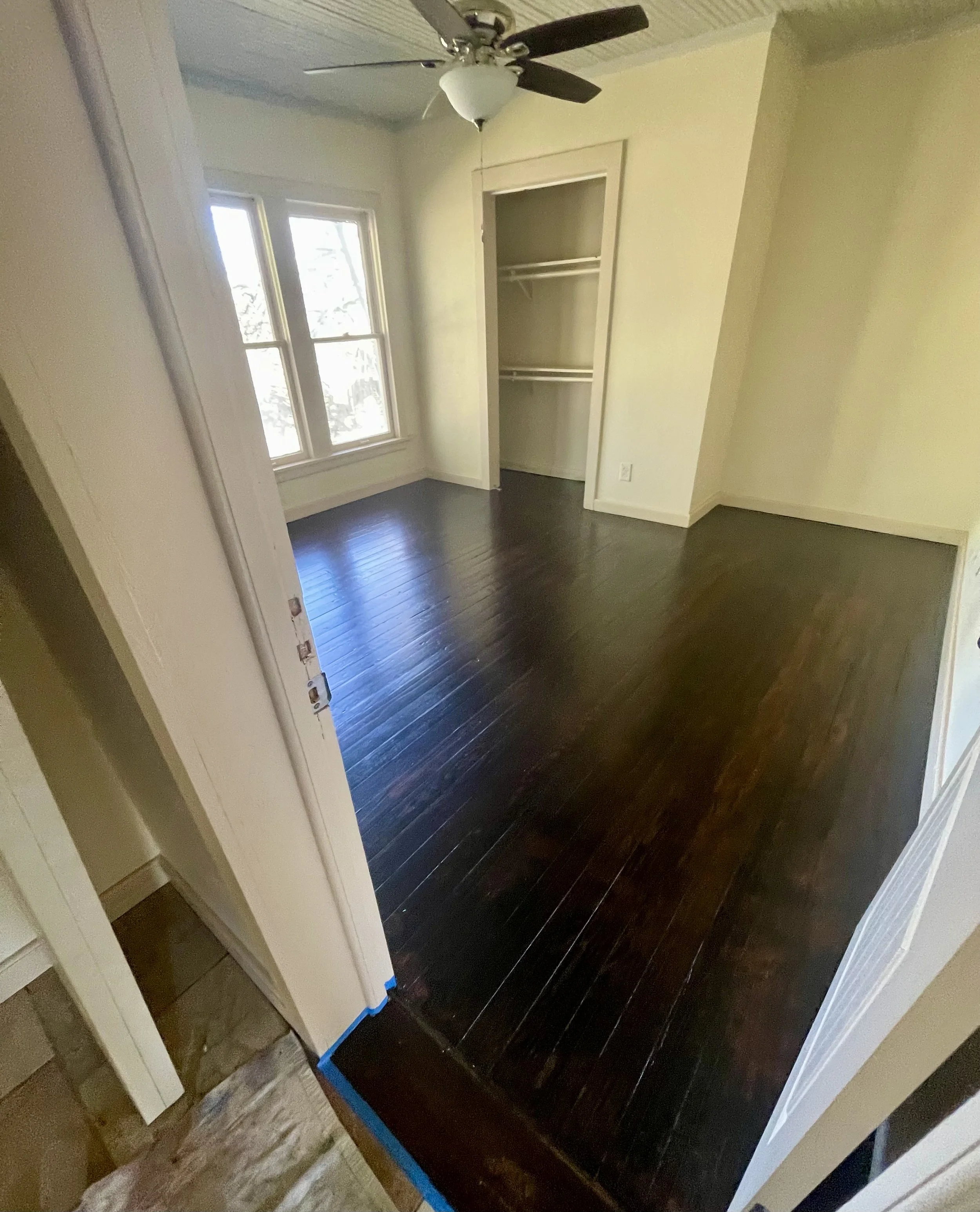 Empty bedroom with dark hardwood floors, a ceiling fan with a light, a window, and an open closet with shelving.