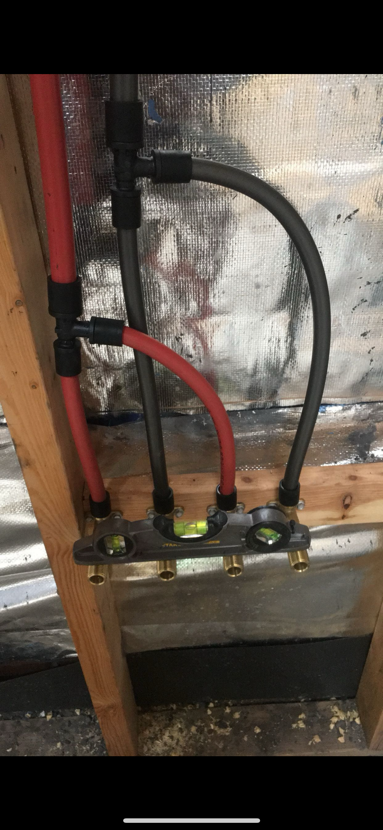 Plumbing pipes with a level tool mounted on a wooden wall with silver insulation behind.