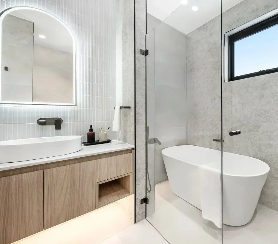 Modern bathroom with a white bathtub, a wooden vanity, a vessel sink, and a large illuminated mirror.