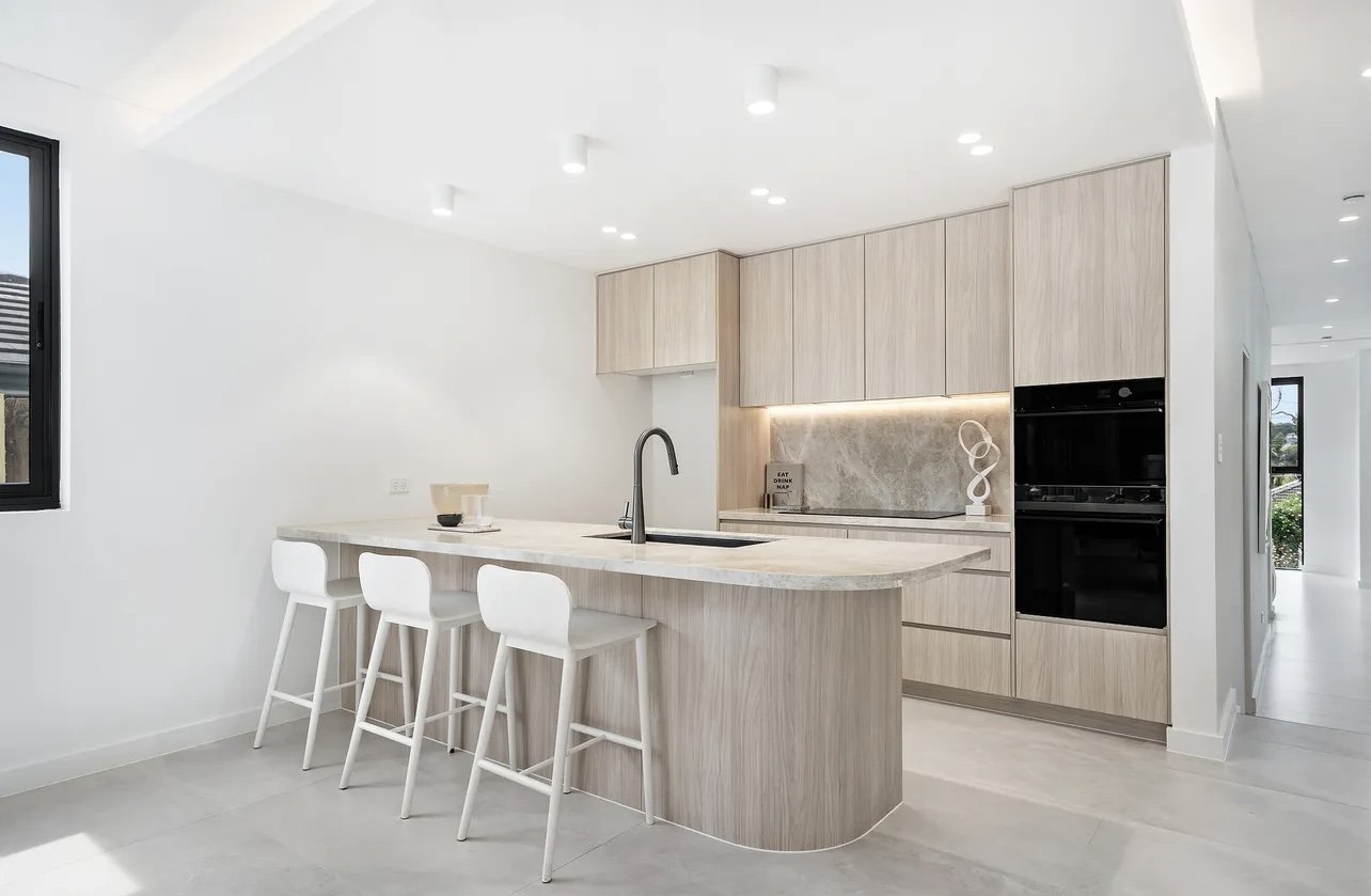 Modern kitchen with light wood cabinets, a white marble island with seating, black appliances, and minimal decor