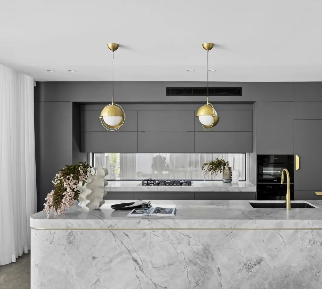 Modern kitchen with gray cabinetry, marble island with gold accents, and pendant lighting.