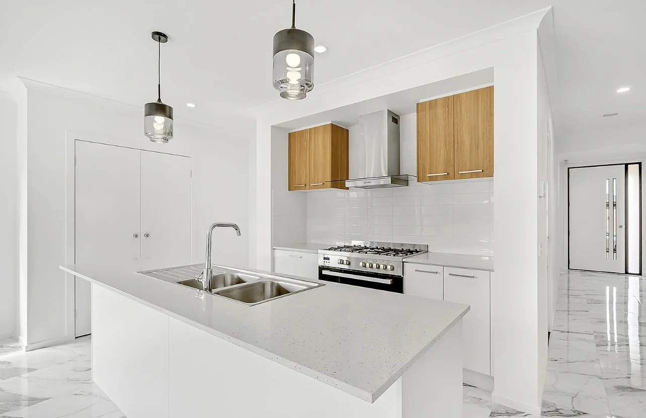 Modern kitchen with white countertops, stainless steel sink, wooden cabinets, and a gas stove.