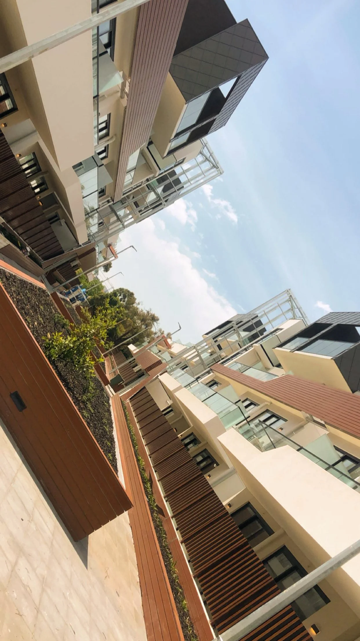 Modern apartment buildings with glass balconies and wooden outdoor seating areas under a partly cloudy sky.