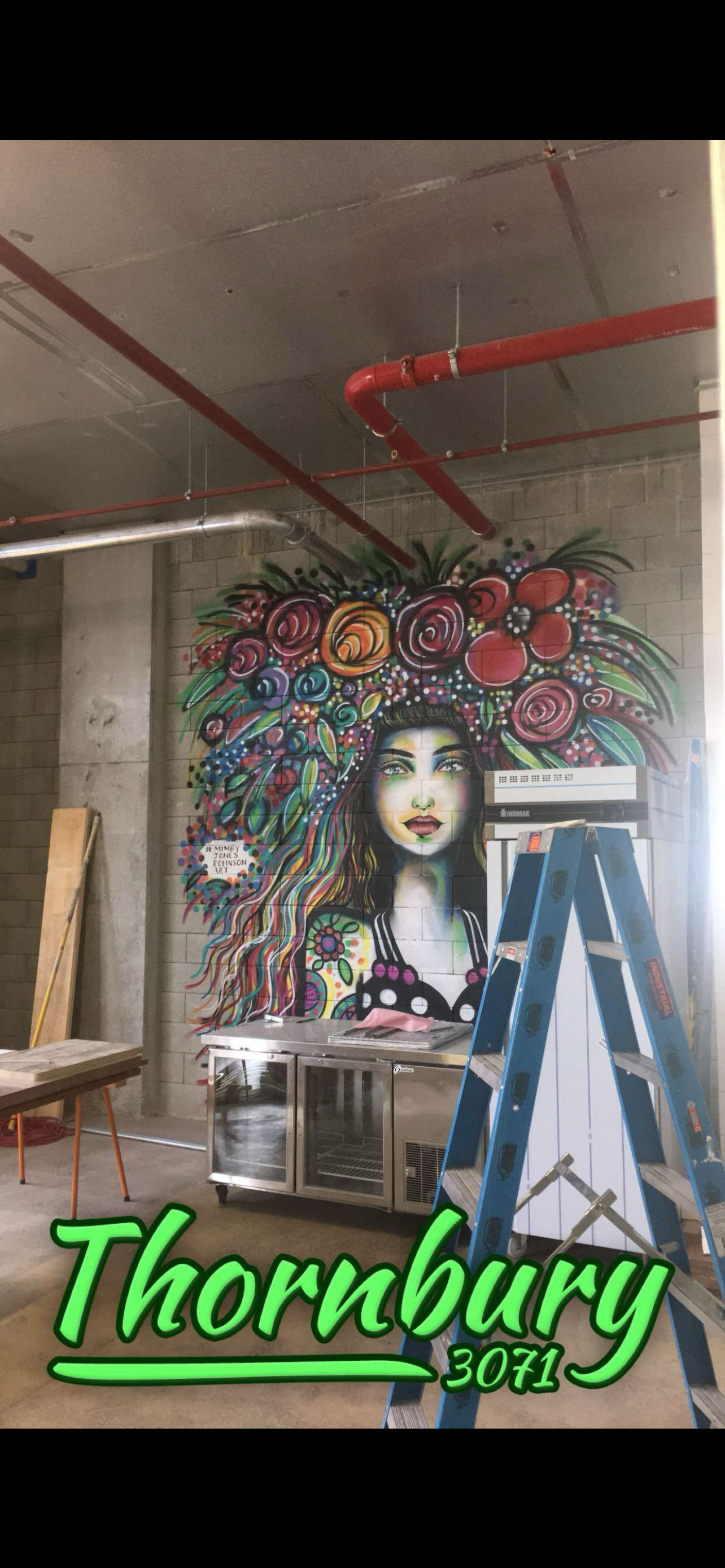 Colorful mural of a woman's face with long hair decorated with flowers and leaves, painted on a brick wall inside a building under construction or renovation.