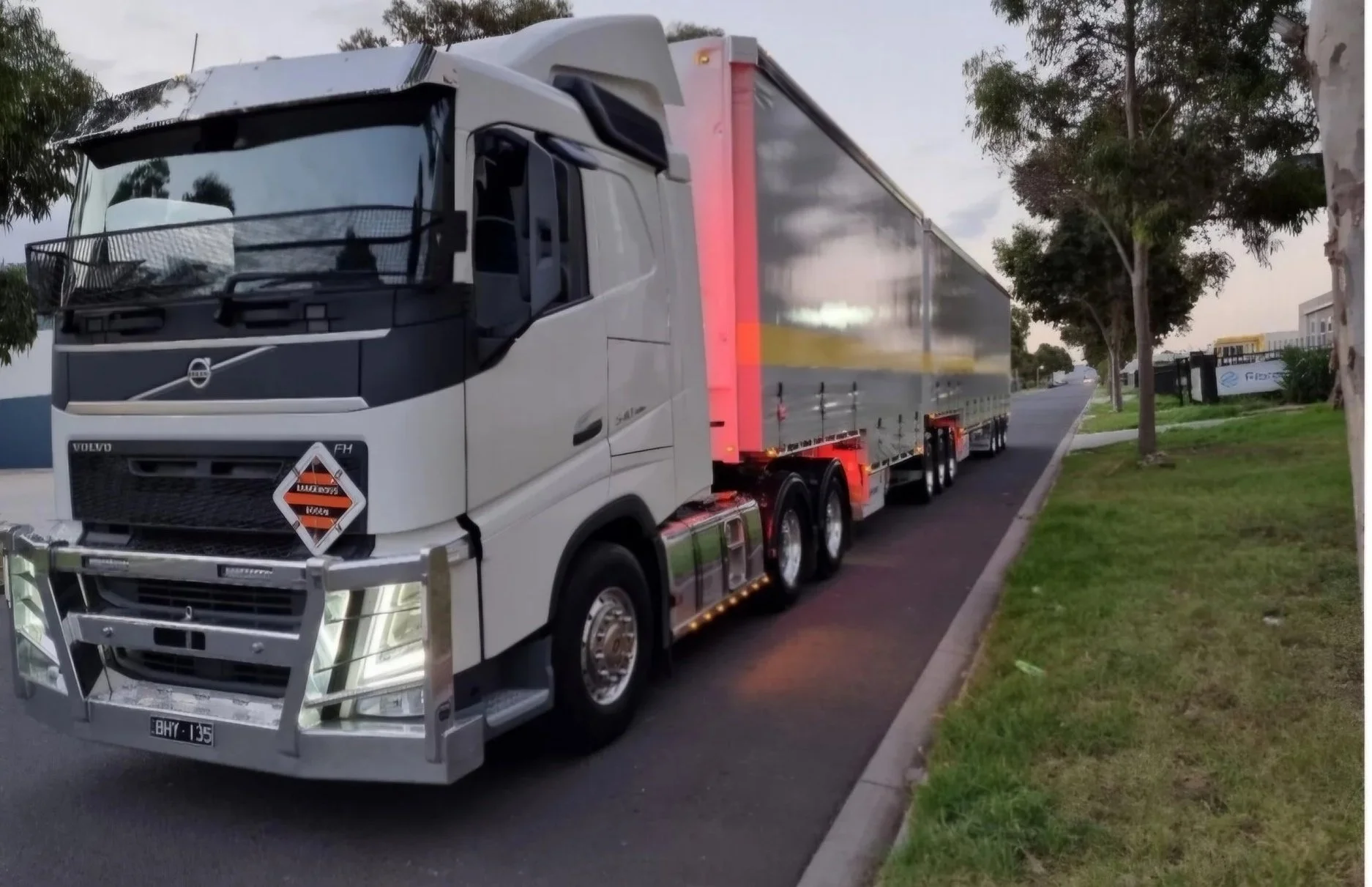 A semi-truck parked on the side of a street with trees and a grassy area.