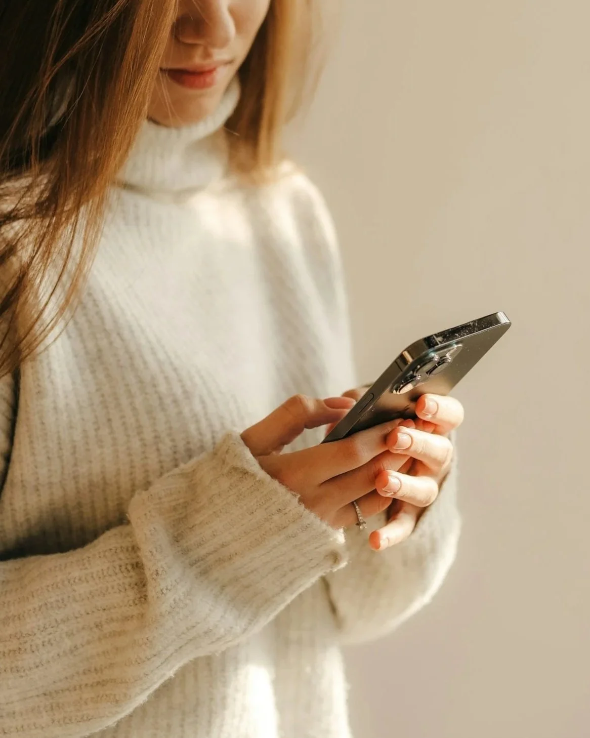 A woman wearing a cream-colored sweater looking at her smartphone.