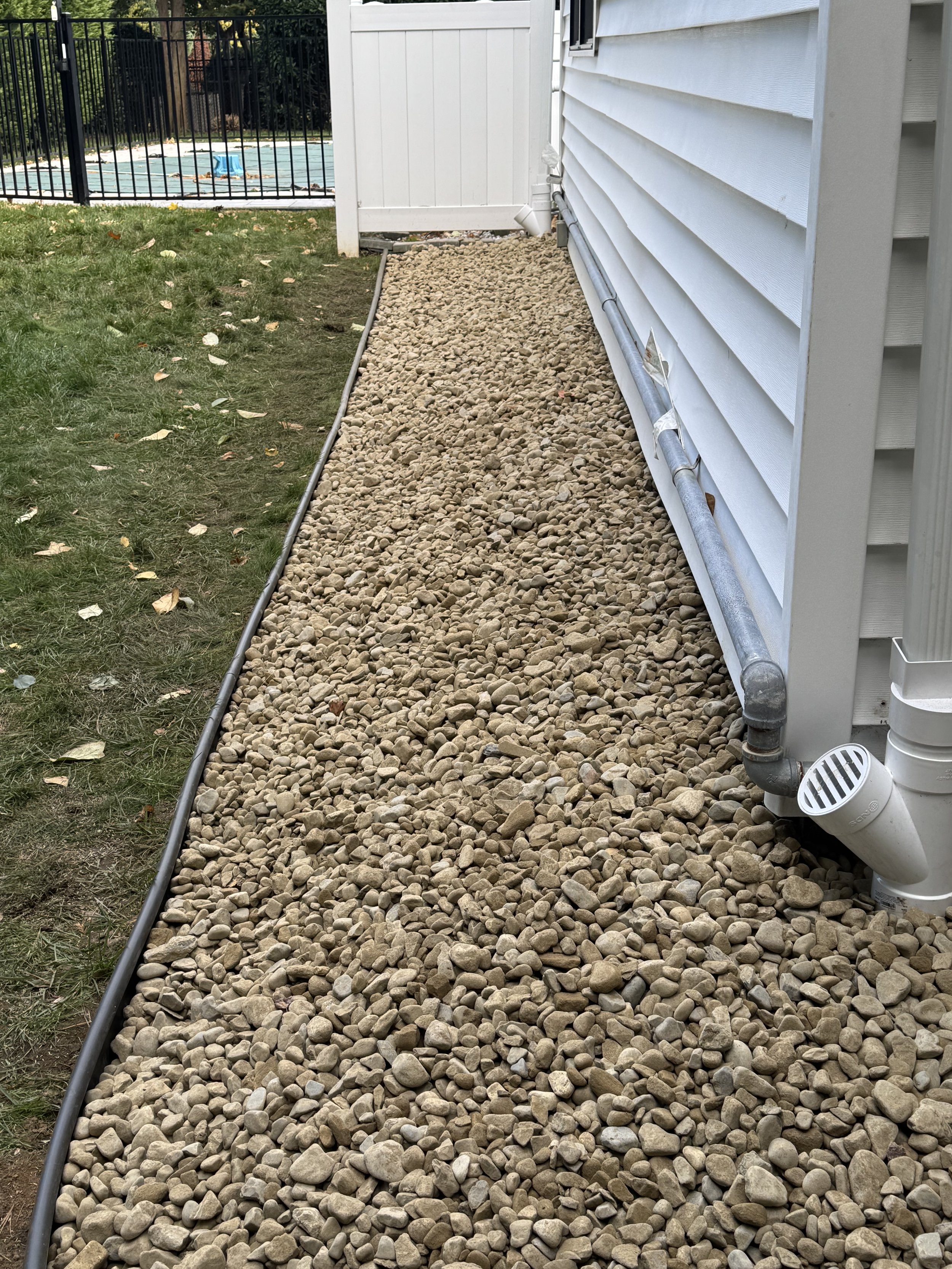Side yard of house with gravel bed, downspout, and garden edging, to keep water away from the foundation of the house.
