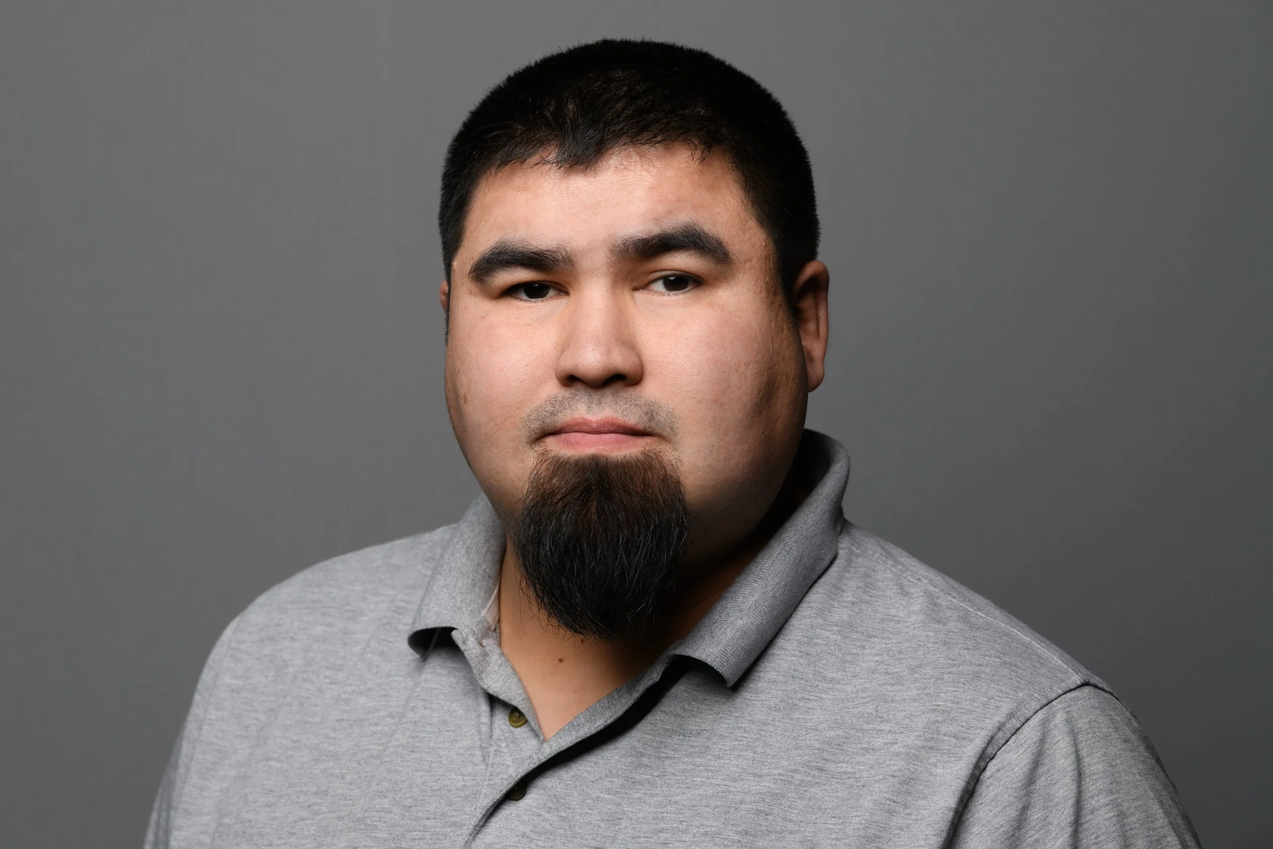 Portrait of a man with short black hair and a goatee, wearing a gray polo shirt, against a gray background.