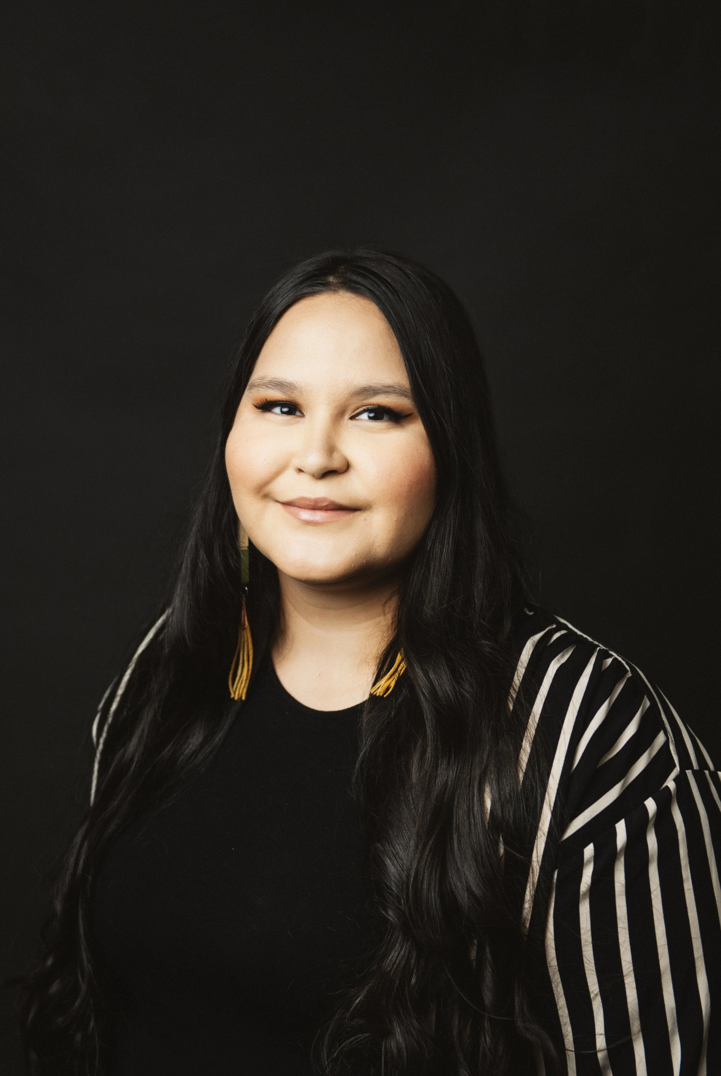 Portrait of a woman with long dark hair, wearing a black top and striped blazer, against a dark background.