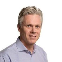 Portrait of a middle-aged man with gray hair wearing a light blue shirt.