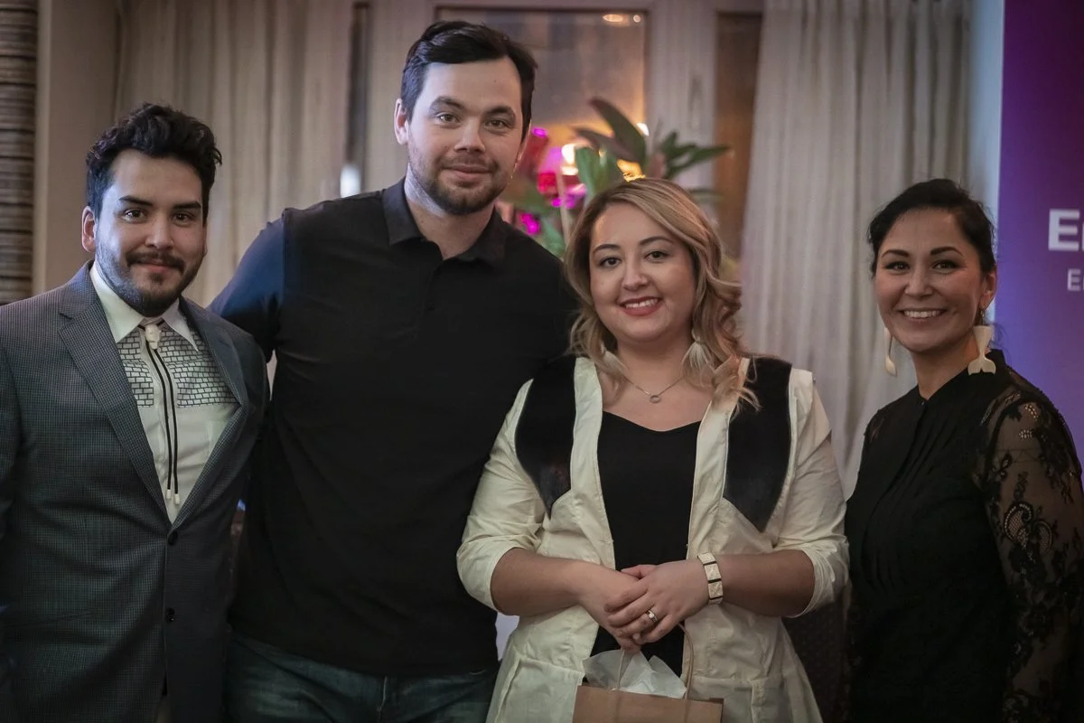Four people standing together and smiling at an indoor event, with a purple banner in the background and floral decorations.