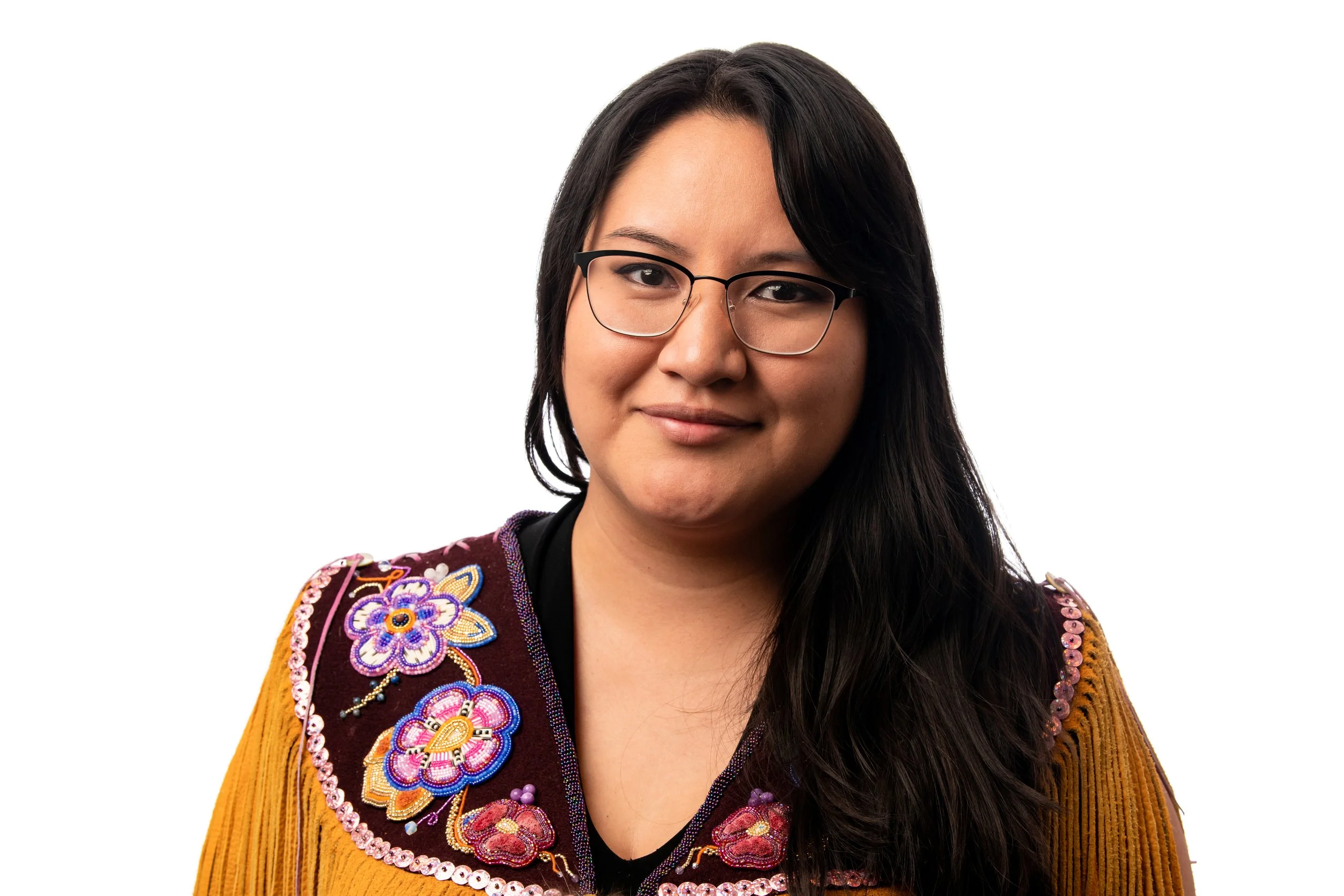 Portrait of a woman with long dark hair, wearing glasses, and a colorful embroidered jacket against a white background.