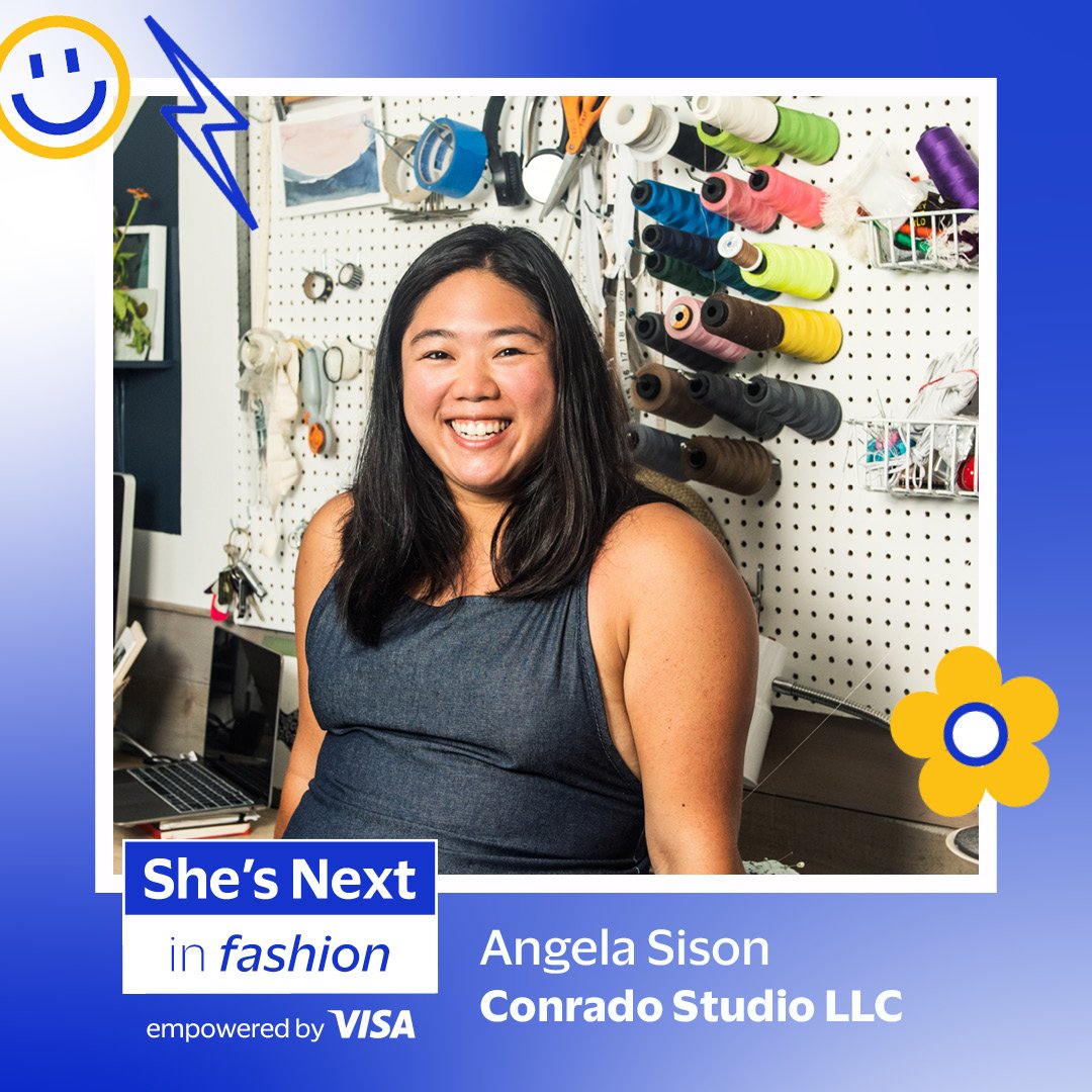 Portrait of Angela Sison smiling in a sewing or design studio, with spools of colorful thread on a pegboard behind her.