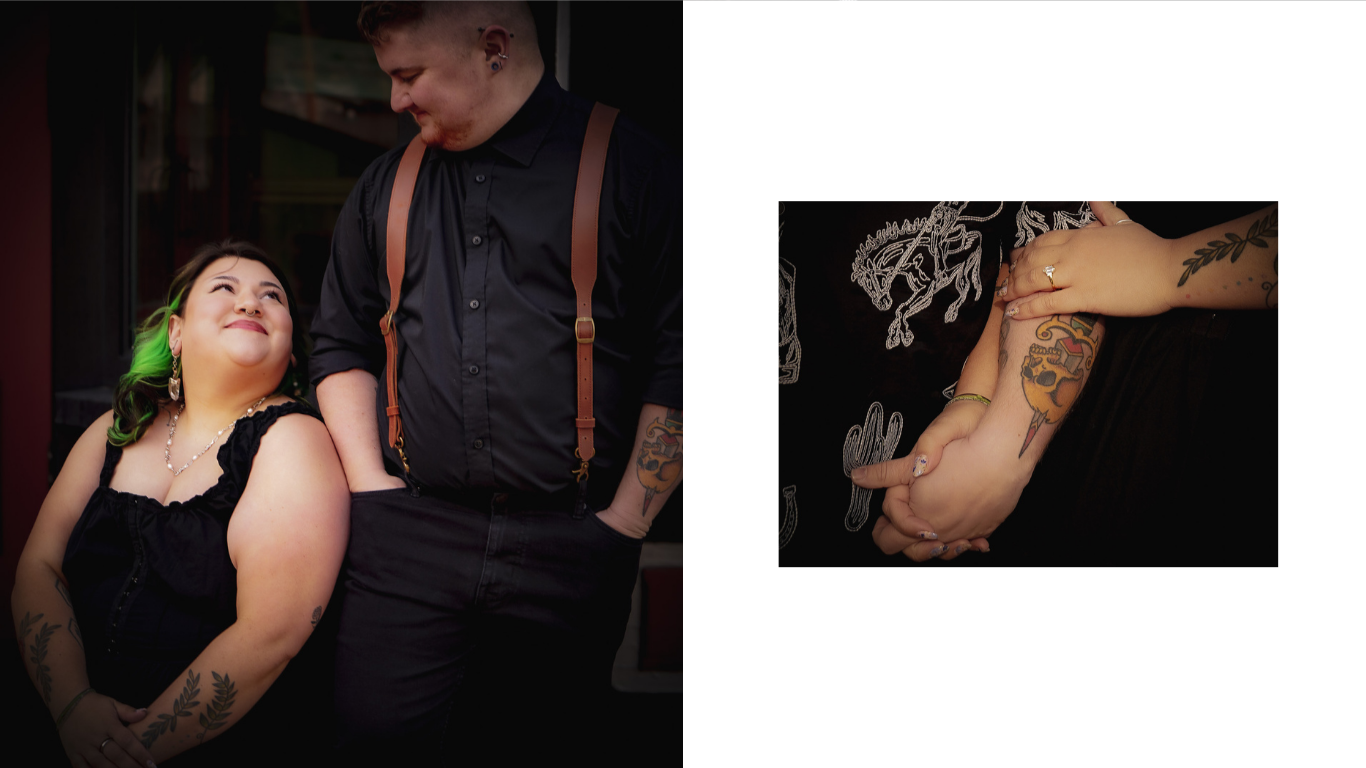 A woman with green hair, tattoos on her arms, and wearing a black dress, sitting next to a man with tattoos on his arm, wearing a black shirt and suspenders, both smiling and holding hands.