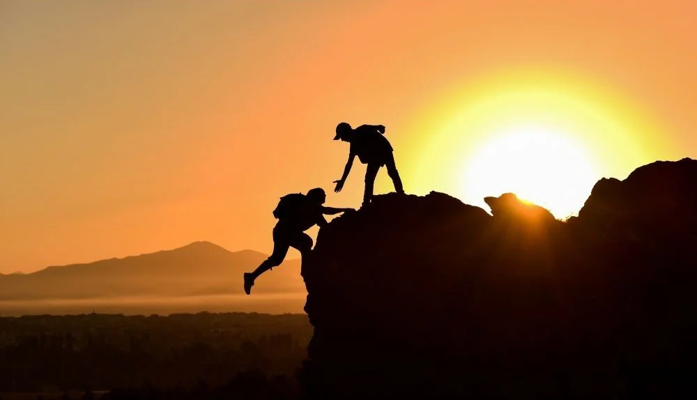 A person lending a hand to help someone up a mountain
