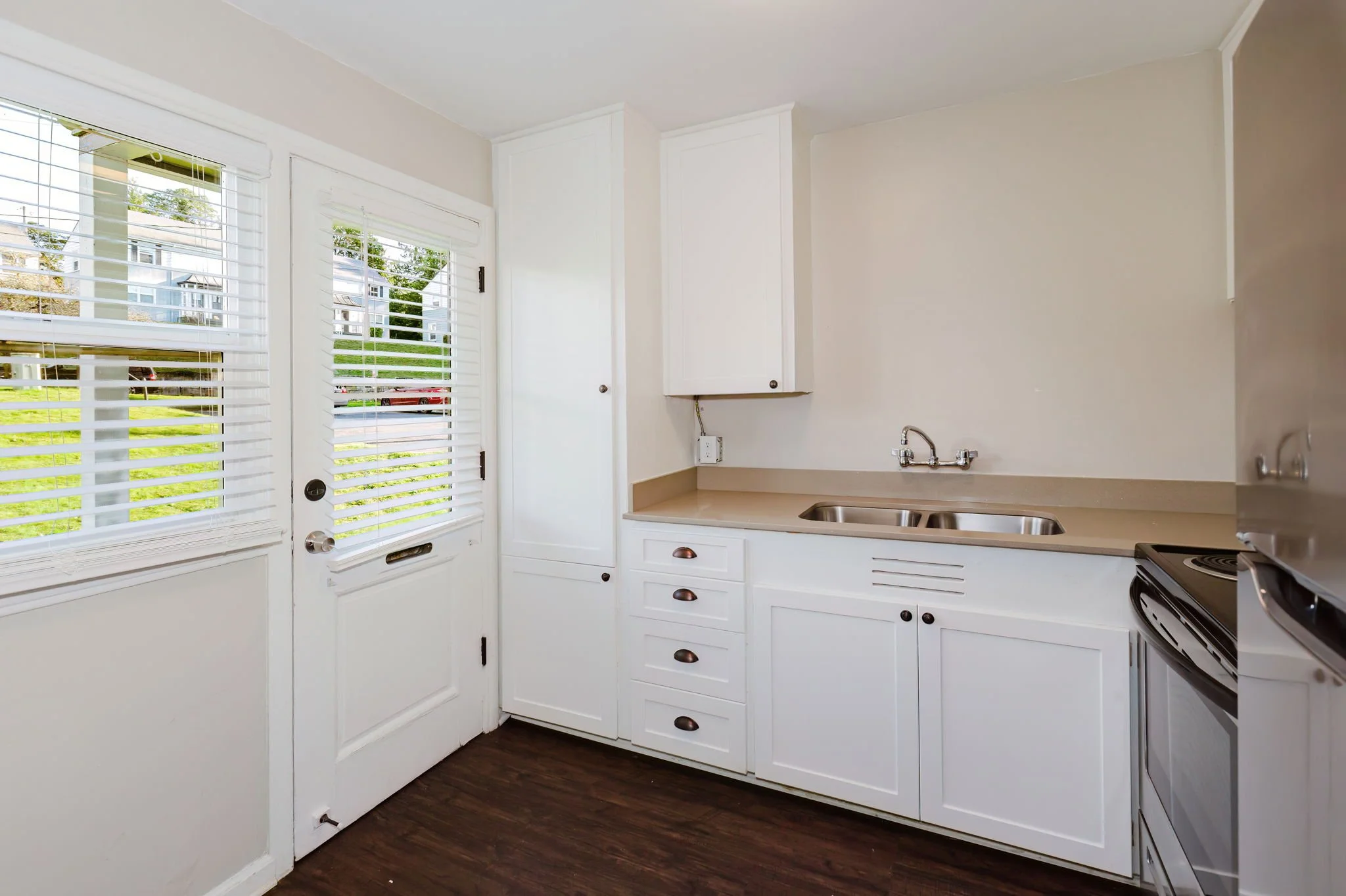 Living room with gray sofa, white pillows, wooden coffee table with plant, hardwood floor, black and white abstract art on walls, large potted monstera plant, doorway leading to another room.