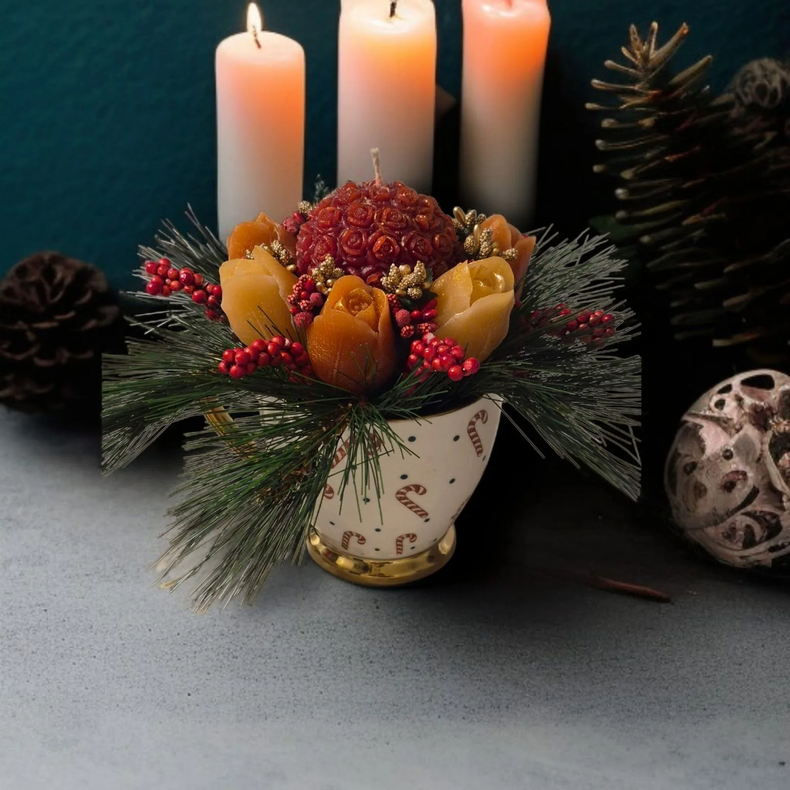 Decorative holiday centerpiece with candles, artificial flowers, pinecones, and greenery in a festive ceramic pot, set against a dark background with Christmas ornaments and candles.