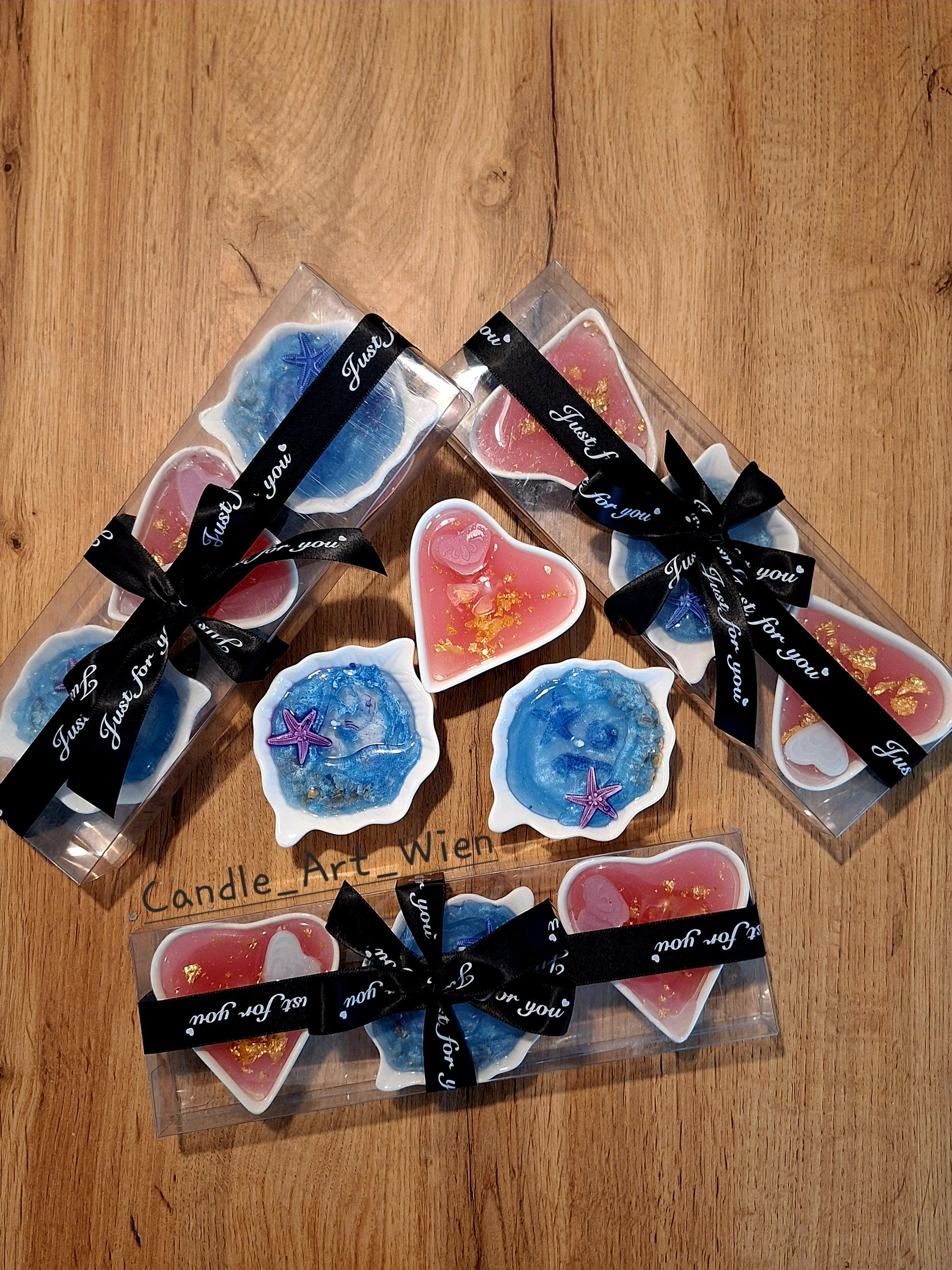 Geschenkboxen und einzelne Teelichter mit Meeresmotiven und Herzformen, dekoriert mit Gold und nur in blauen, roten und weißen Farben, auf einem Holztisch