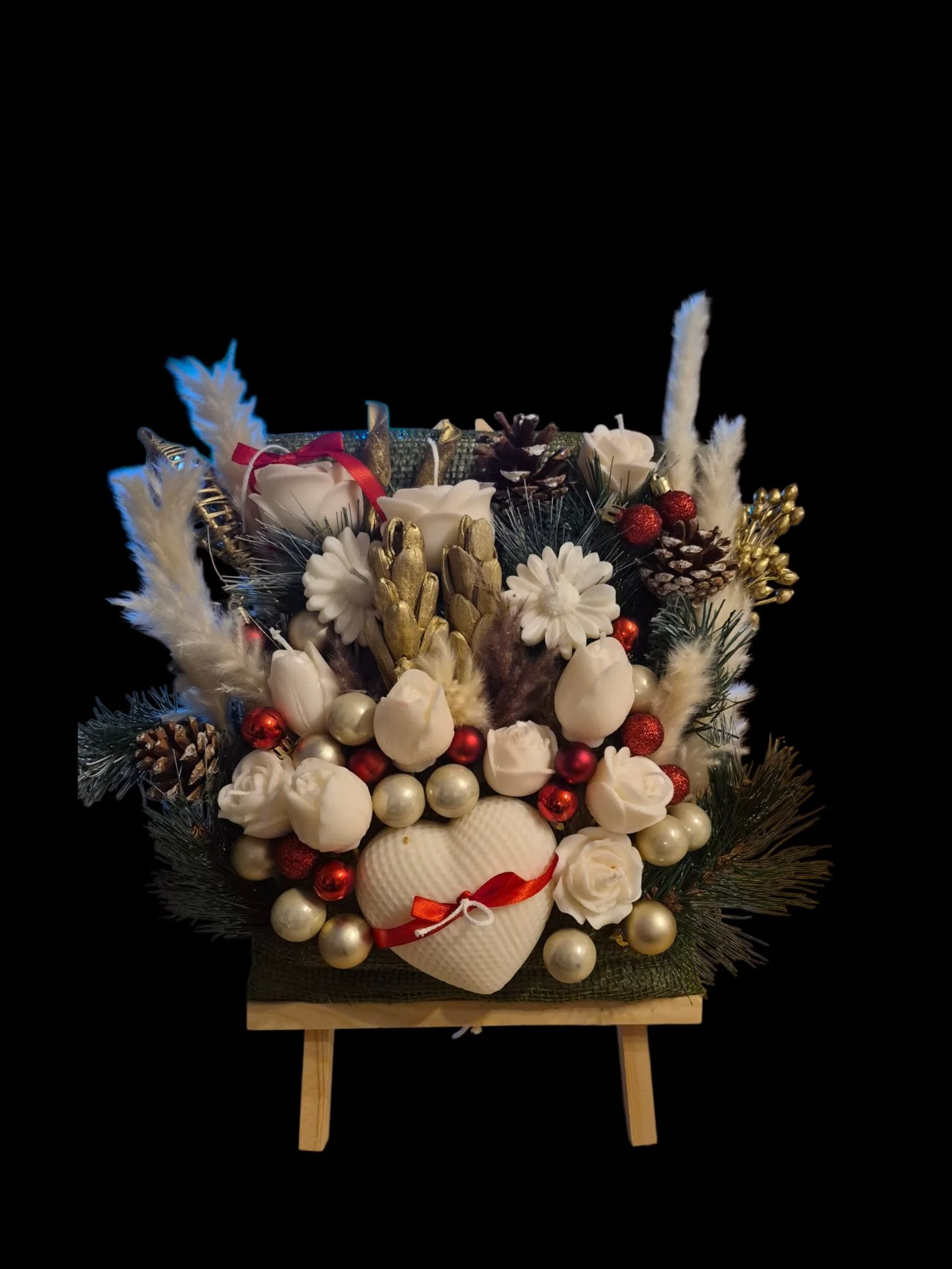 Weihnachtsdeko mit weißen Blumen, roten und goldenen Kugeln, Zapfen, Federn und Herz auf einem kleinen Holzständer