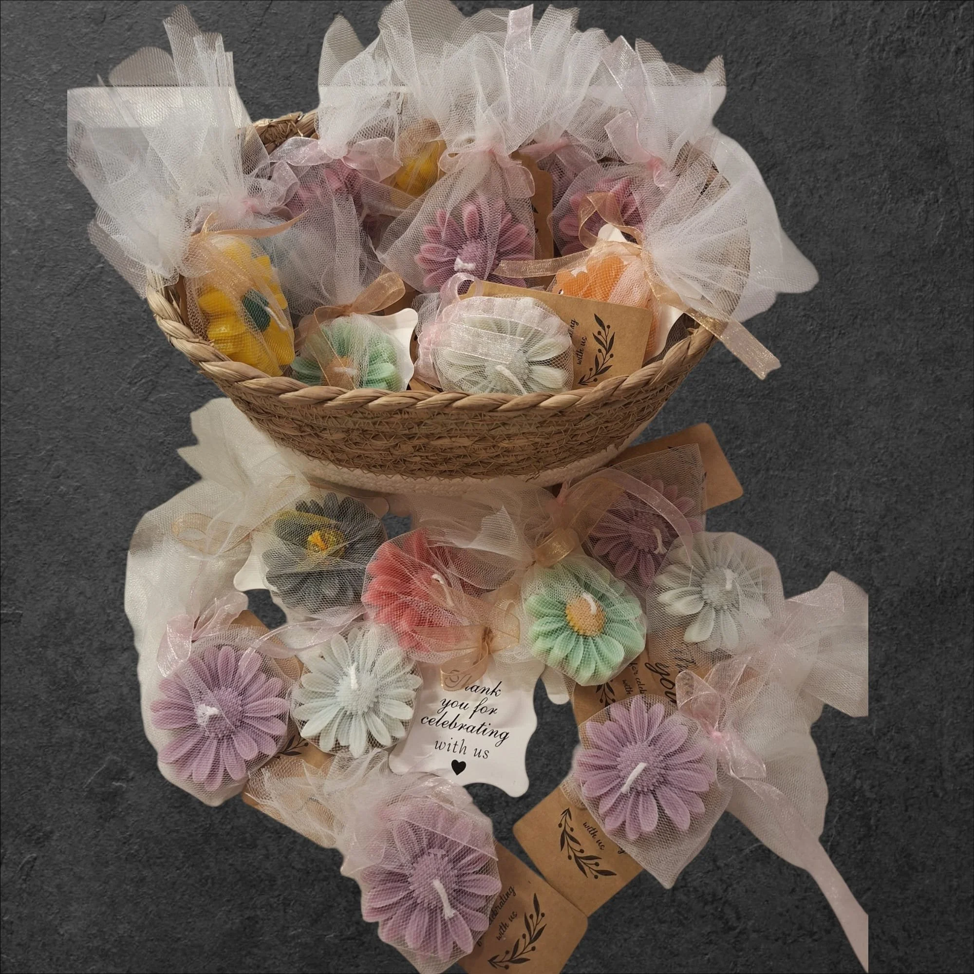 Geschenkeshaufen mit bunten, gerollten Kerzenblumen in Tüllbeuteln, mit Dankekarten auf dunklem Hintergrund.