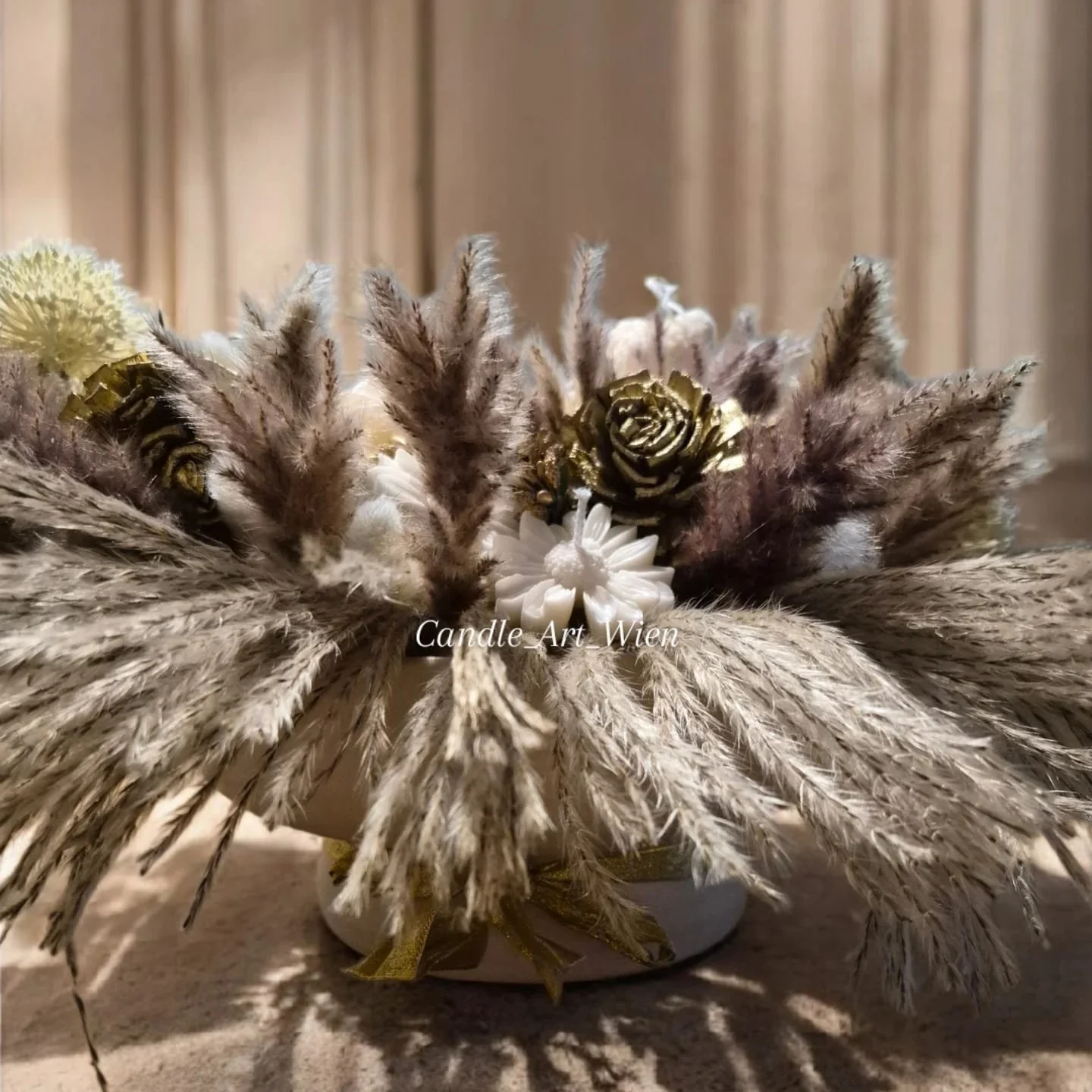 Dekoratives Blumenarrangement mit weißen und goldenen Kerzen Blumen, getrockneten Gräsern und Federn in einer weißen Schale