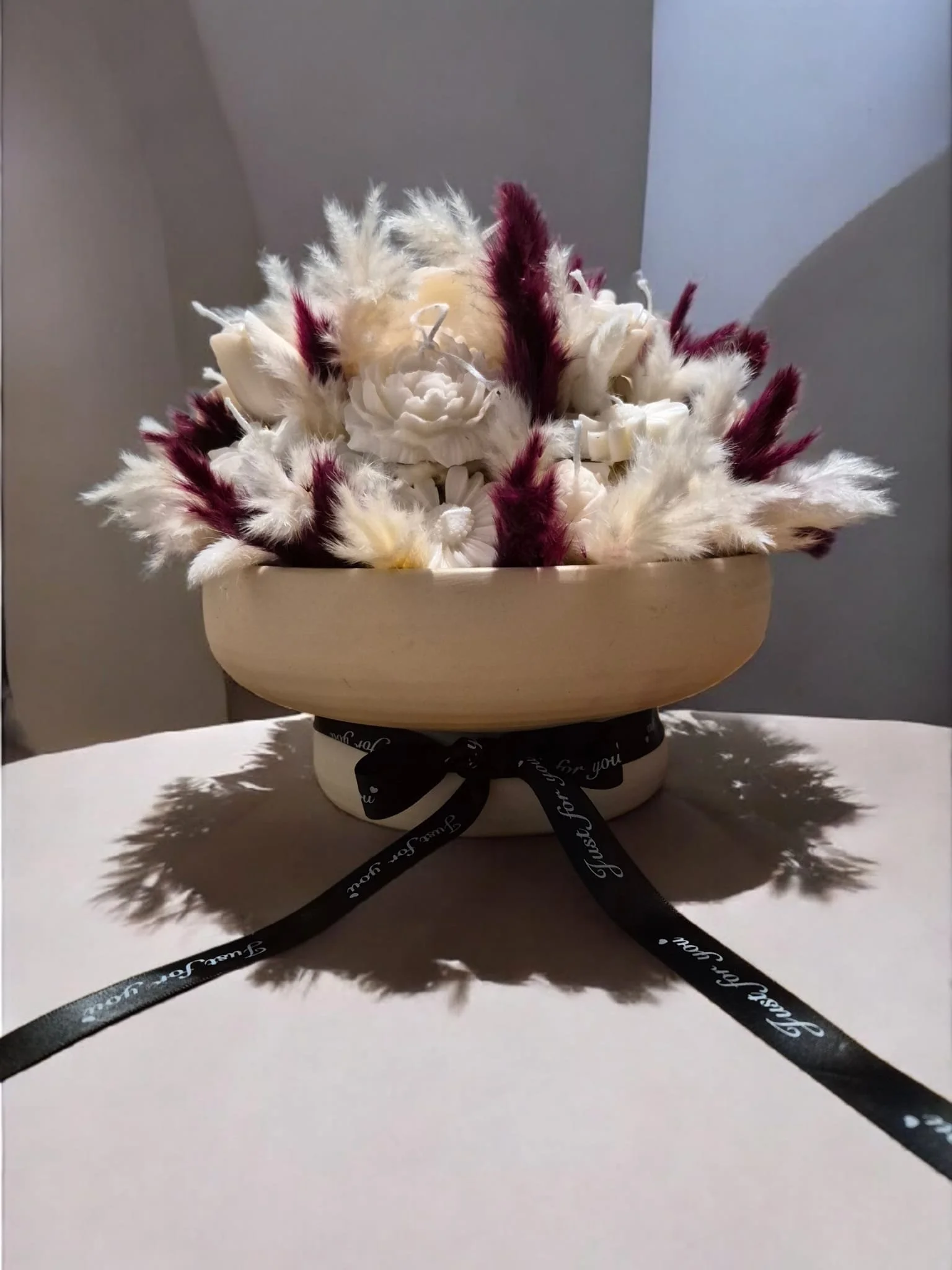 Blumenstrauß in einer weißen Schale mit schwarzer Schleife, der auf einem weißen Tisch steht.