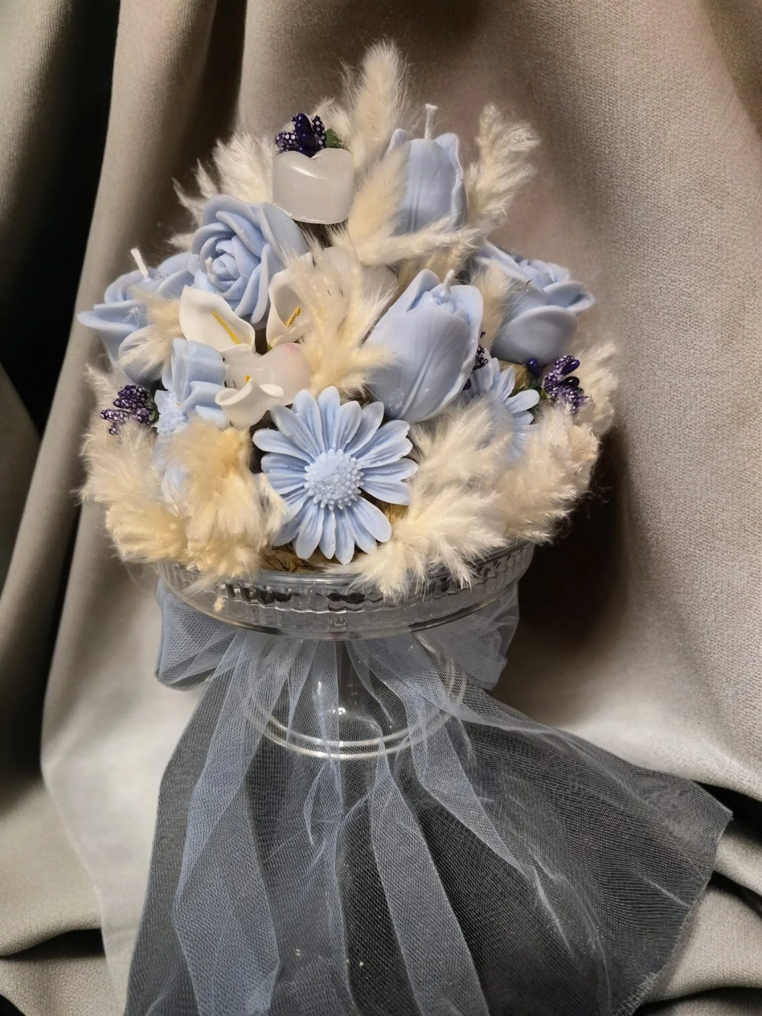 Blumenarrangement mit blauen und weißen Kerzen - Blumen in einer Glasschale, verziert mit Tüll und Federn.
