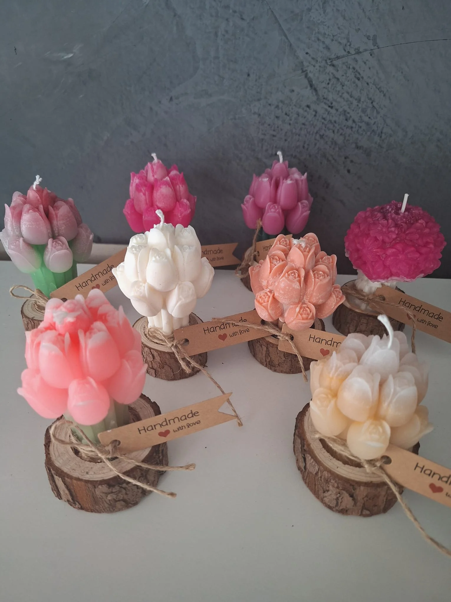 Bunte handgemachte Kerzen in Blumenform auf Holzscheiben, verziert mit Schnur und Kärtchen mit der Aufschrift 'Handmade with love'