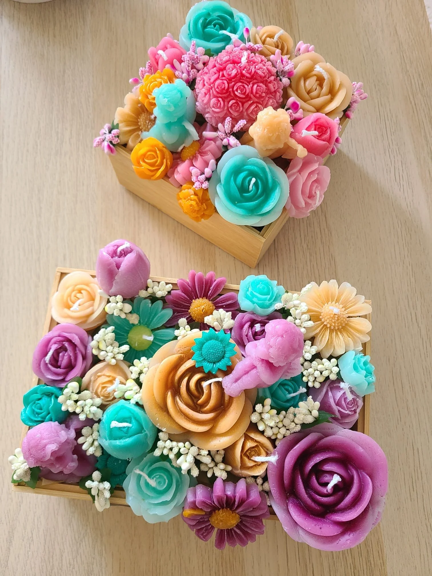 Two wooden boxes filled with colorful soap flowers arranged in decorative bouquets on a light wood surface.