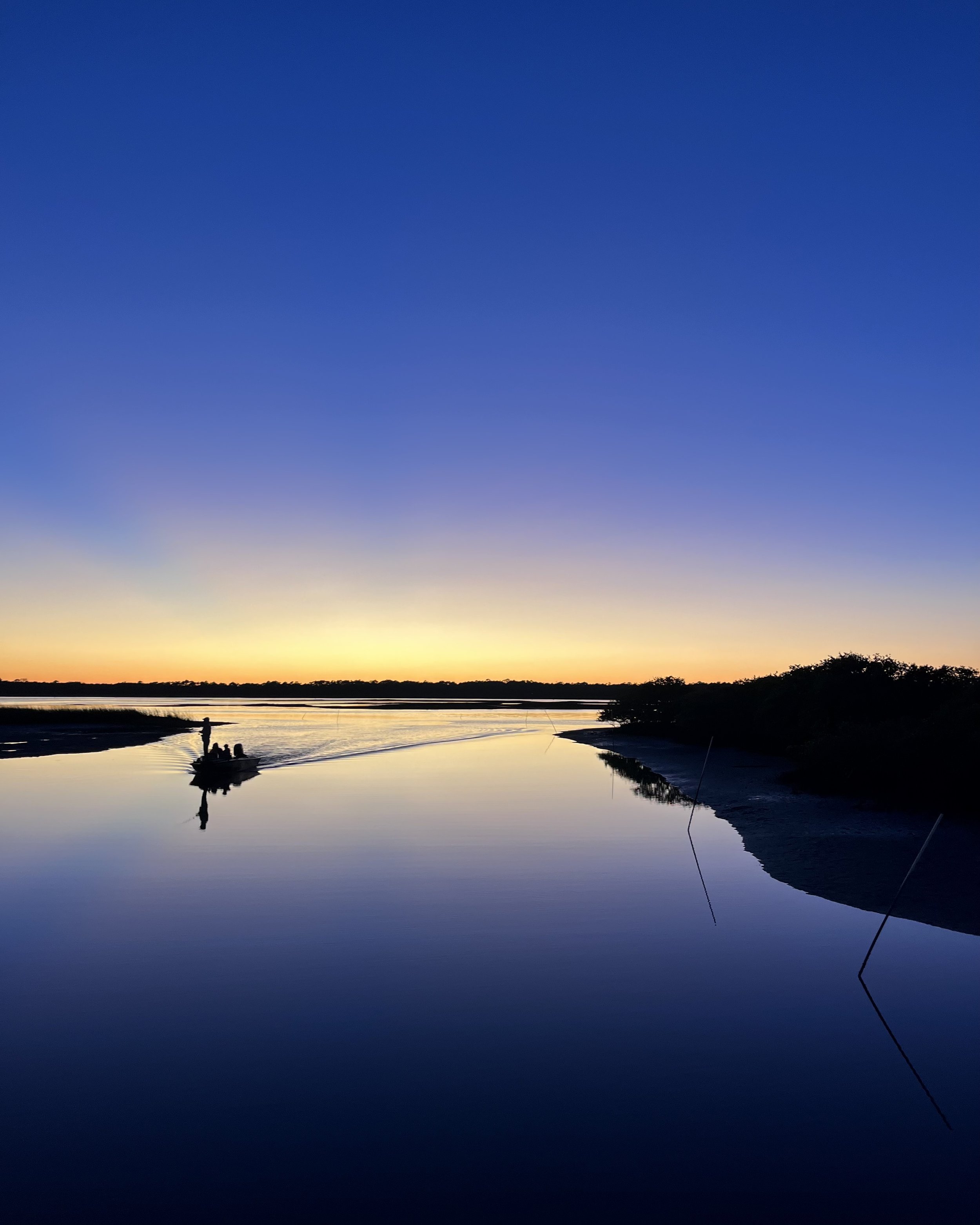 Sunset over calm marsh water near Butler Beach, with silhouetted shoreline and reflections in the water.