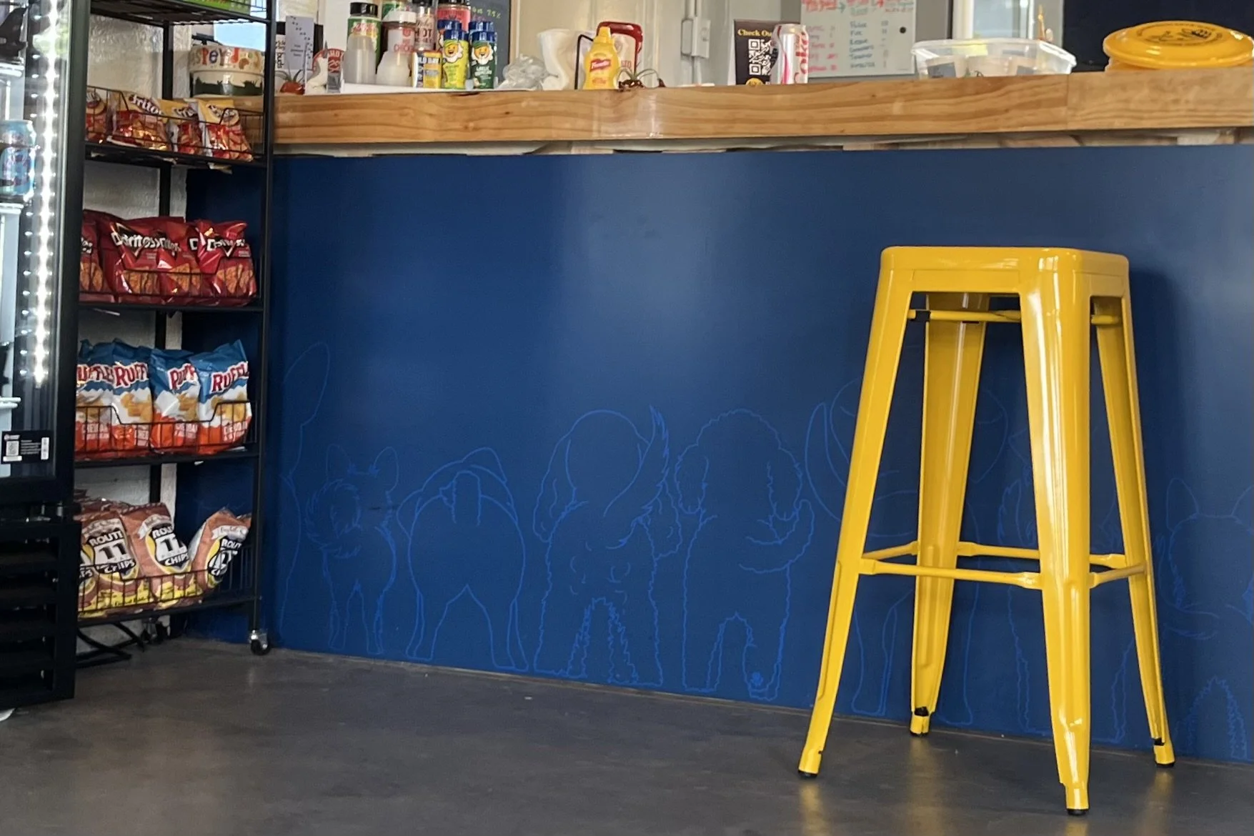 Blue taphouse bar with a yellow stool and dog illustrations inside The Barking Barley in Fredericksburg.