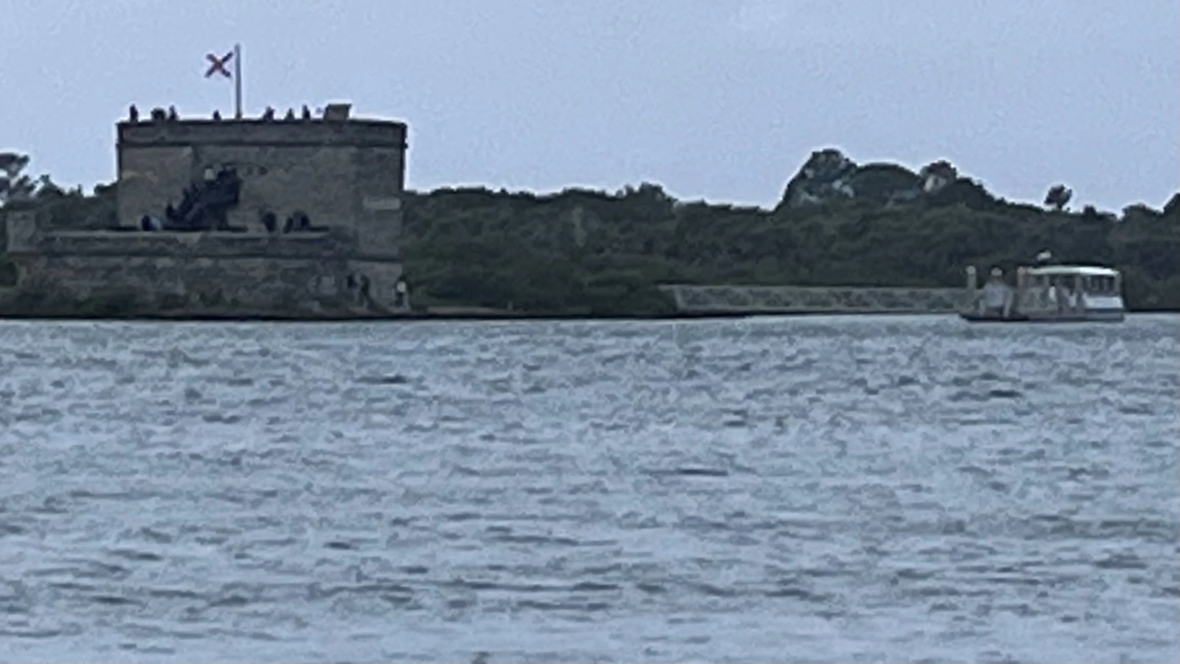 View across the water toward Fort Matanzas, with the stone fort, flag, and a small boat nearby.