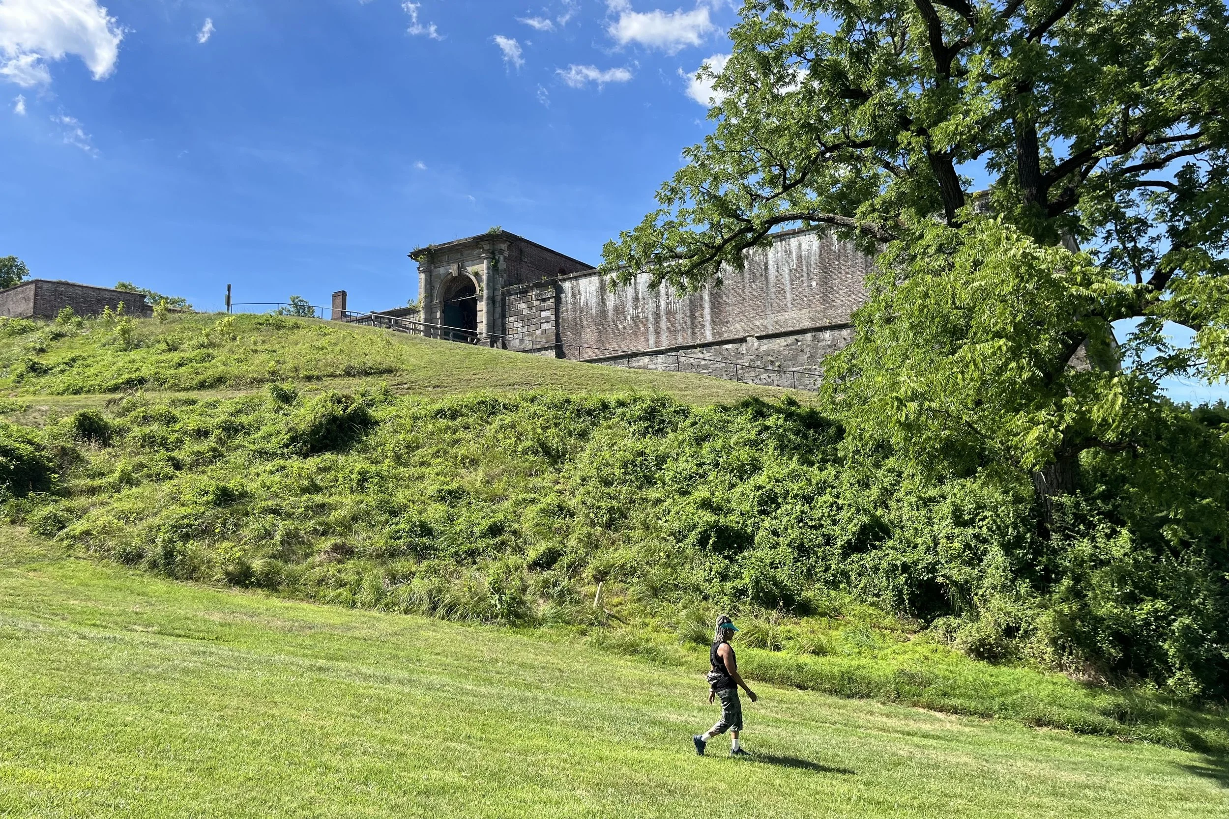 Fort Washington viewed from the grassy lower grounds, with the historic stone entrance and walls visible above the hillside.