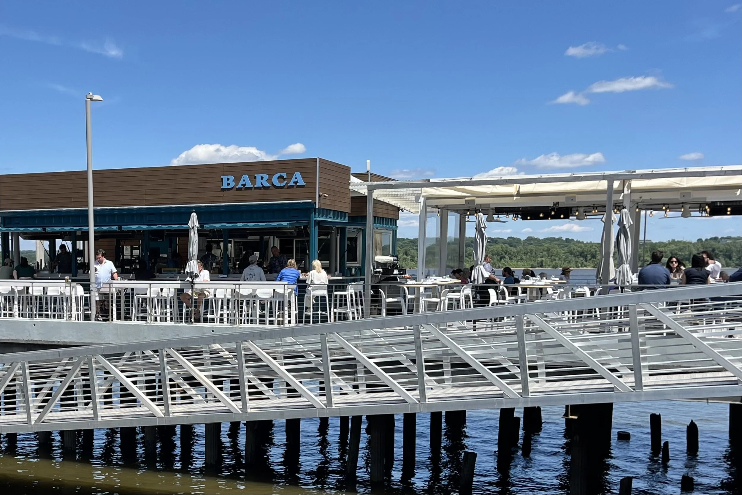 Outdoor waterfront dining at BARCA Pier & Wine Bar in Old Town Alexandria with tables extending over the Potomac River.