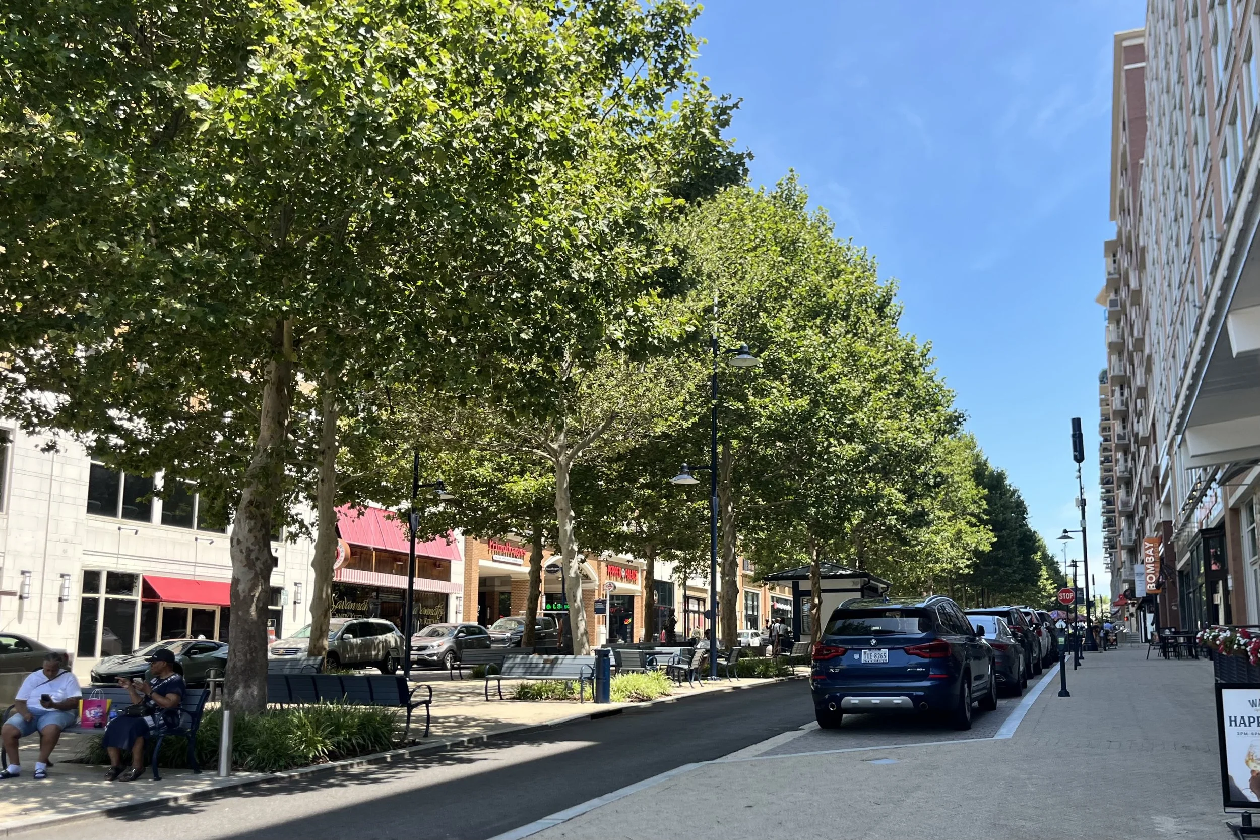 Tree-lined street with restaurants and shops at National Harbor on a sunny afternoon.