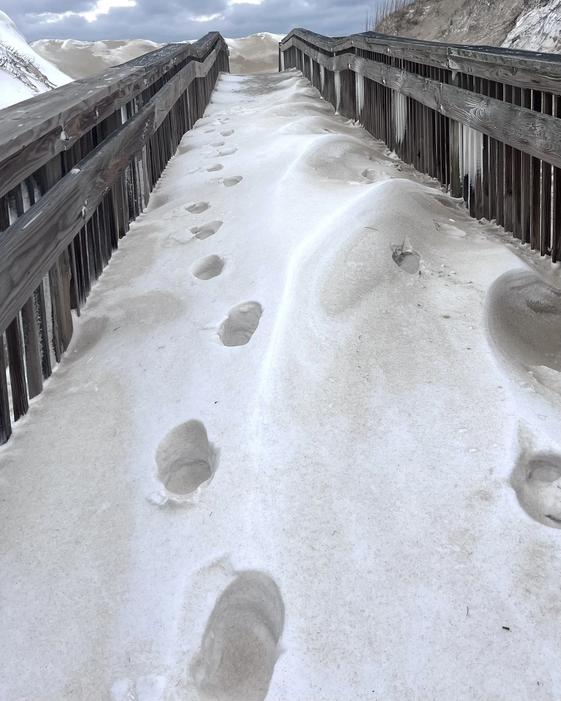 Snow-covered boardwalk through coastal dunes during a winter storm in the Outer Banks.
