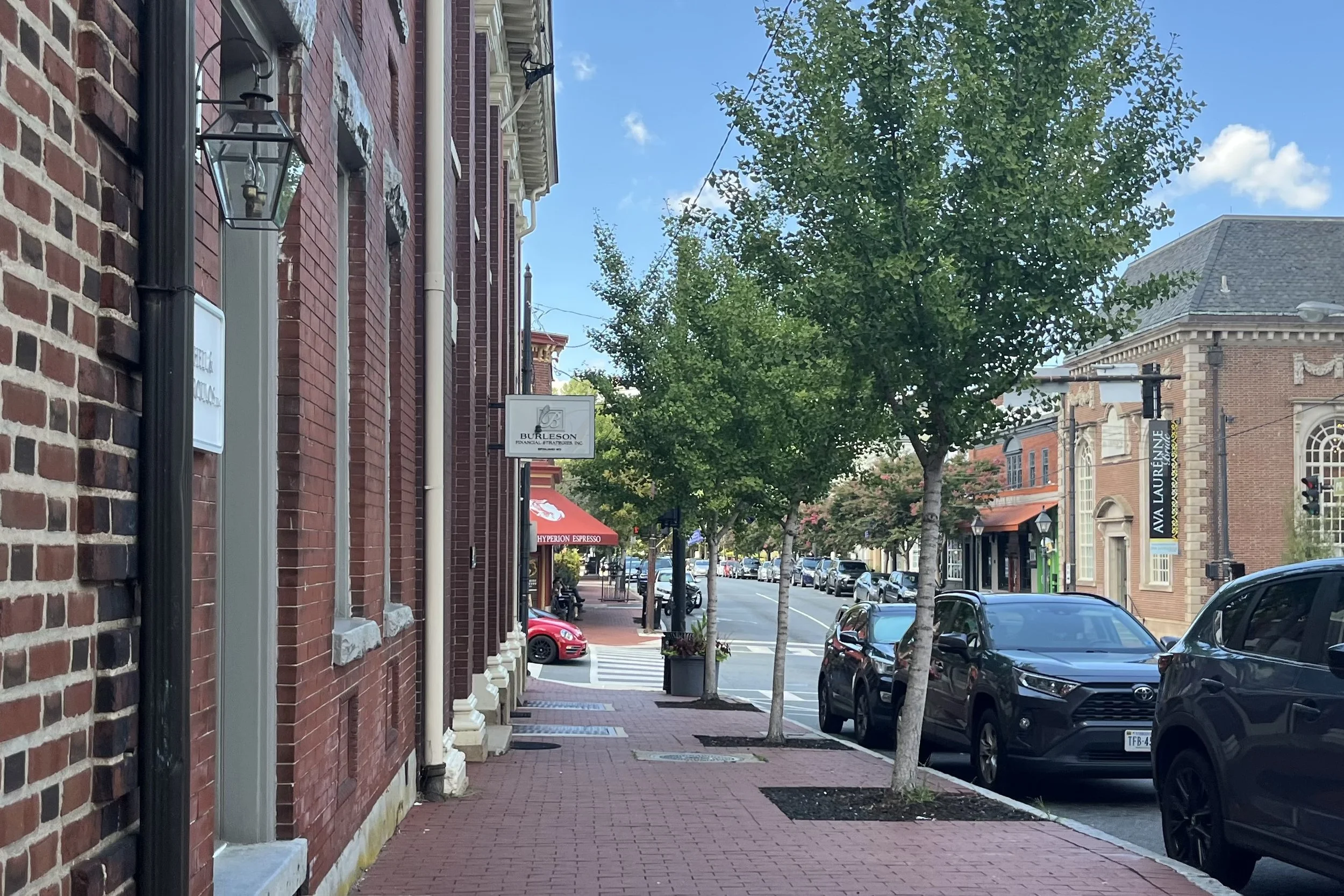Wide red-brick sidewalk lined with historic buildings and trees in downtown Fredericksburg, Virginia.