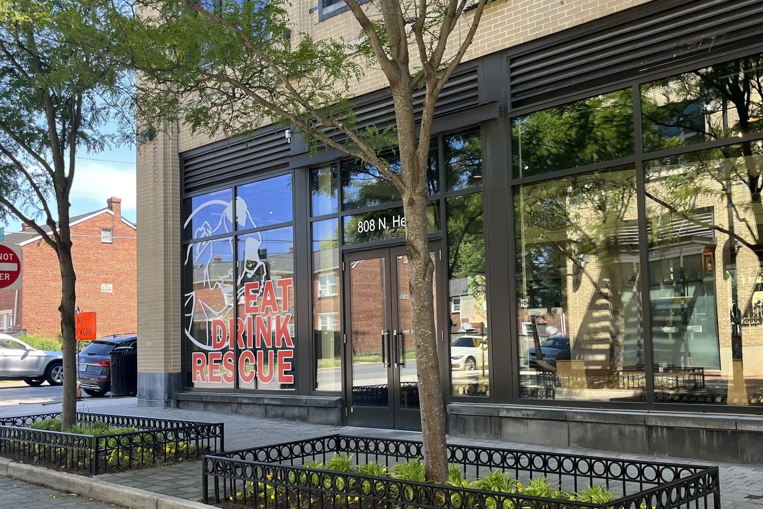 Exterior of Lost Dog Cafe in Old Town Alexandria with Eat Drink Rescue window signage and tree-lined sidewalk.