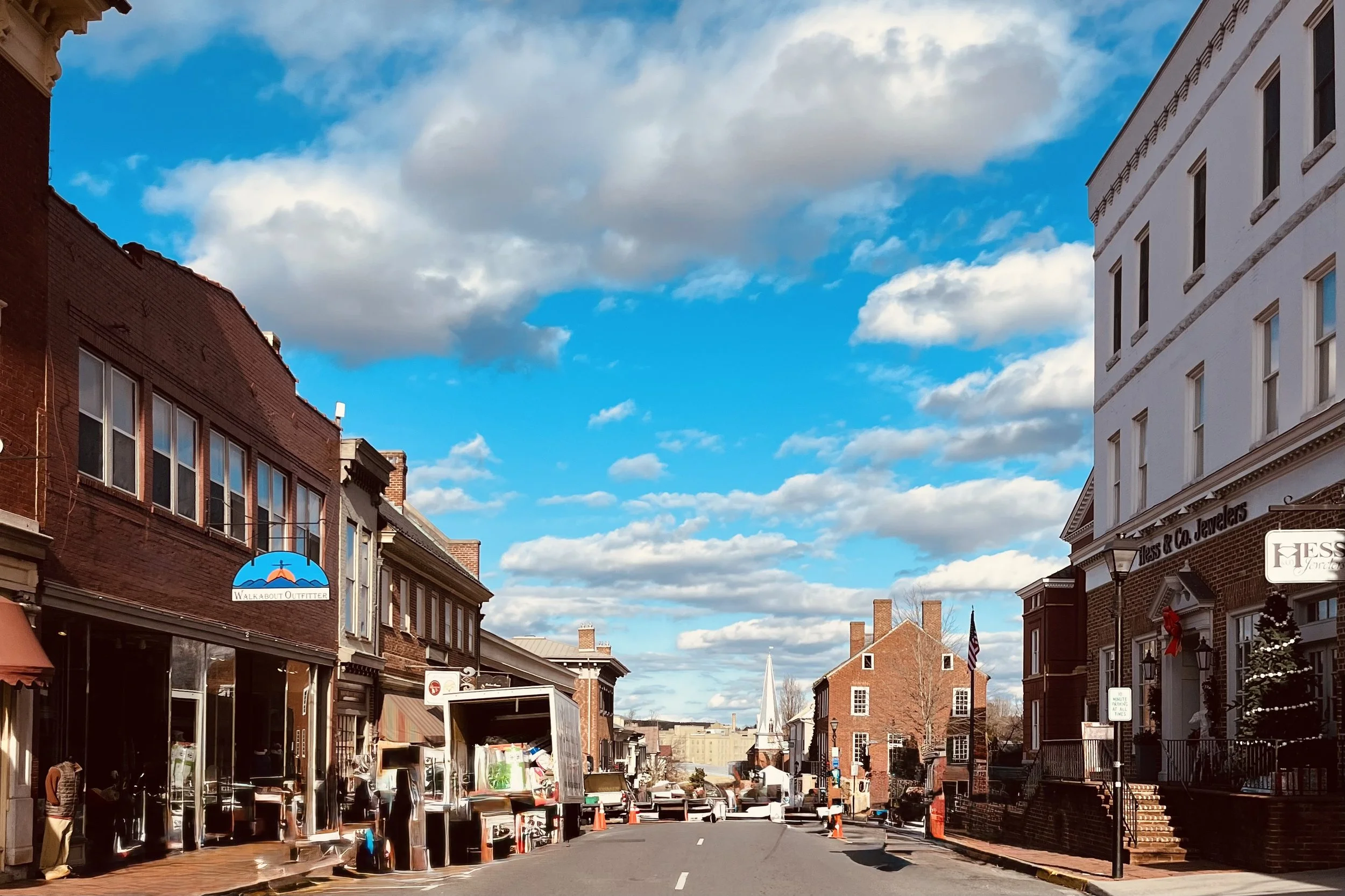 Historic storefronts lining a downtown street in Lexington, Virginia, beneath a partly cloudy sky.
