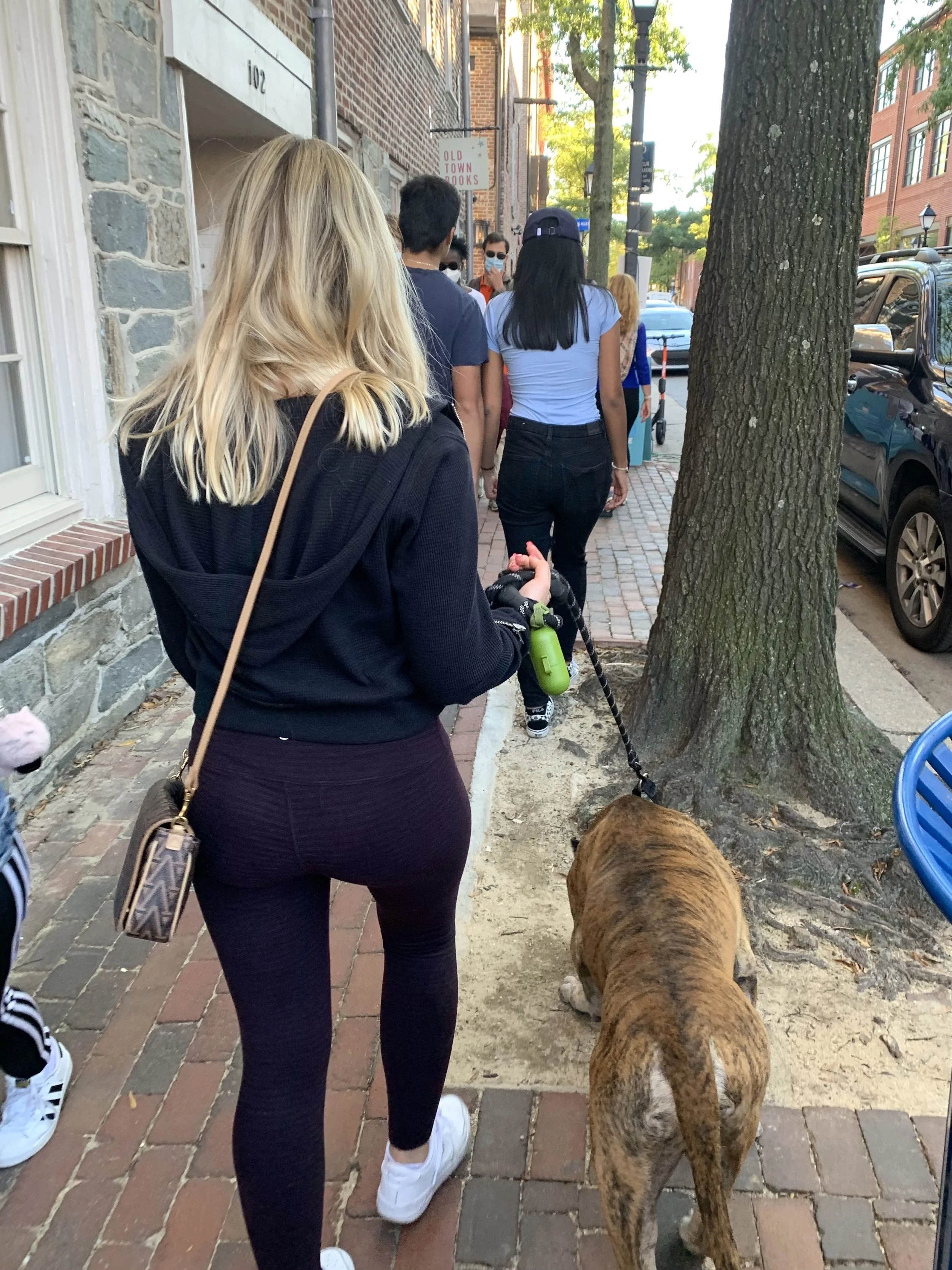 Crowded narrow sidewalk with people, a tree, and objects limiting space, creating a compressed walking path