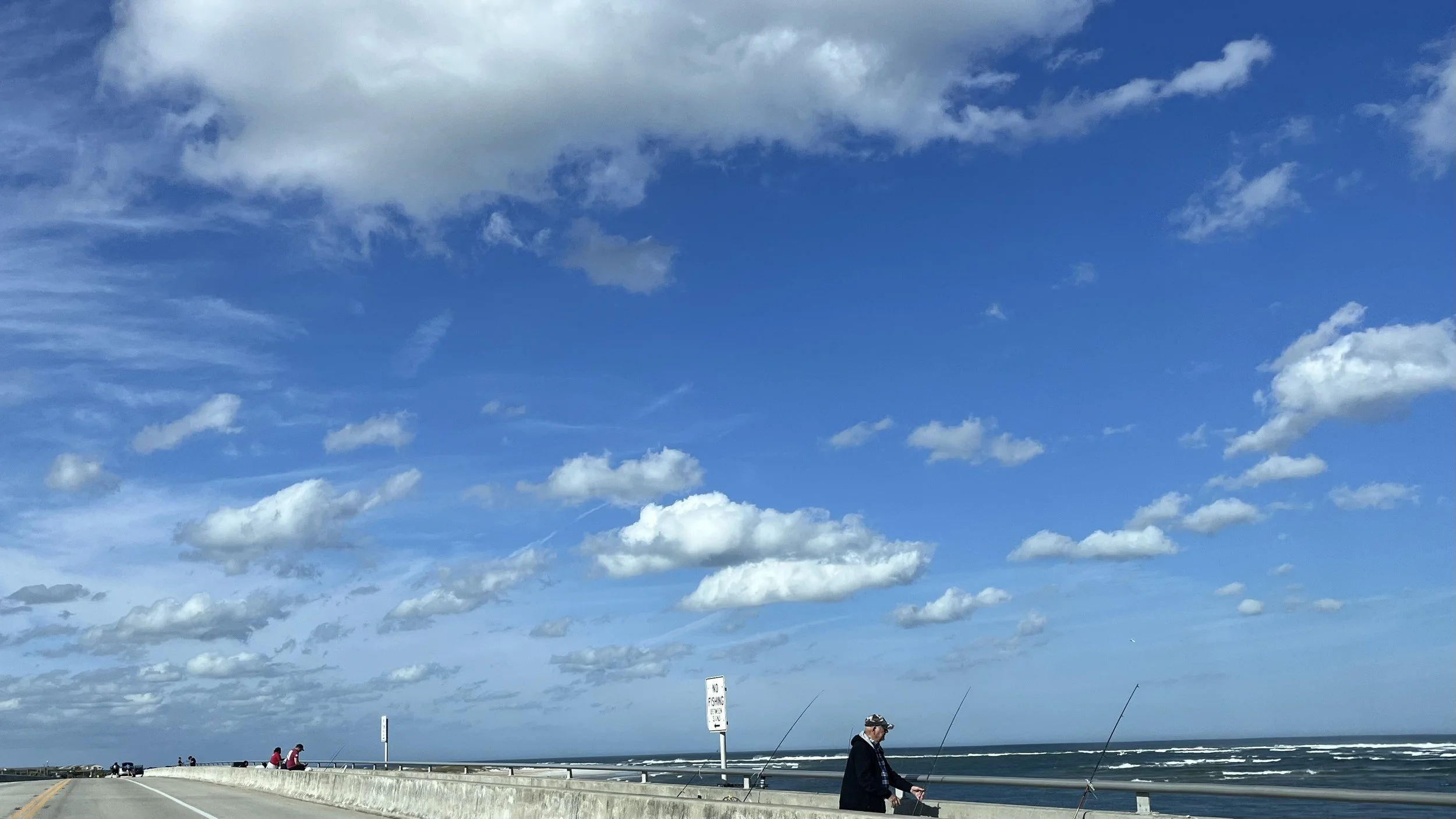 People fishing from the bridge at Matanzas Inlet, with open ocean and blue sky.