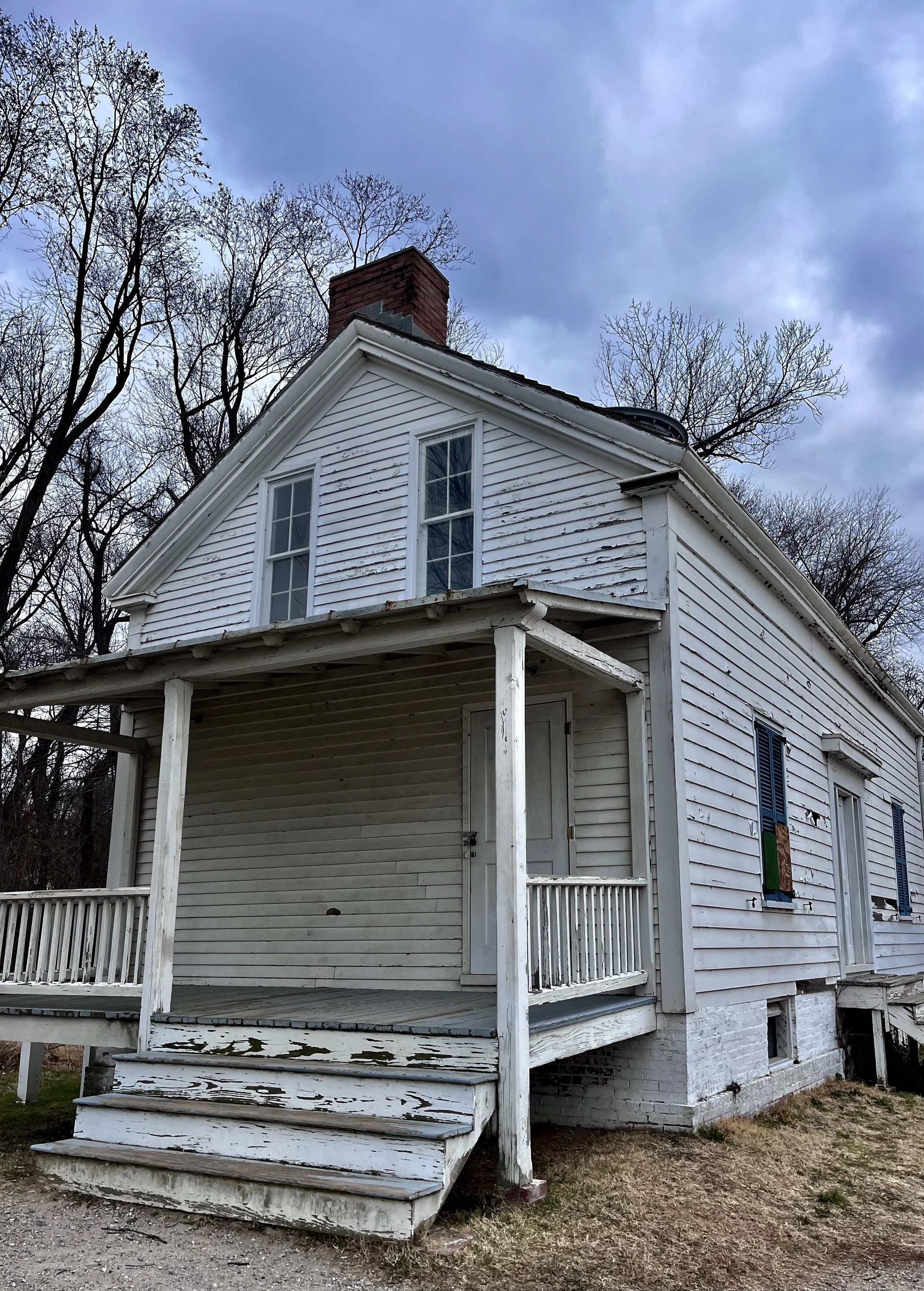 A small white historic house with a front porch and chimney, set among leafless trees in Old Town Alexandria.